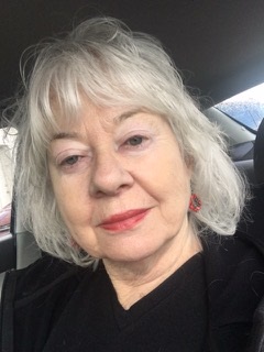 Kathleen Tate wears a black shirt as she smiles at the camera. Tate, a retired nurse, has silvery gray hair that frames her face with bangs. 