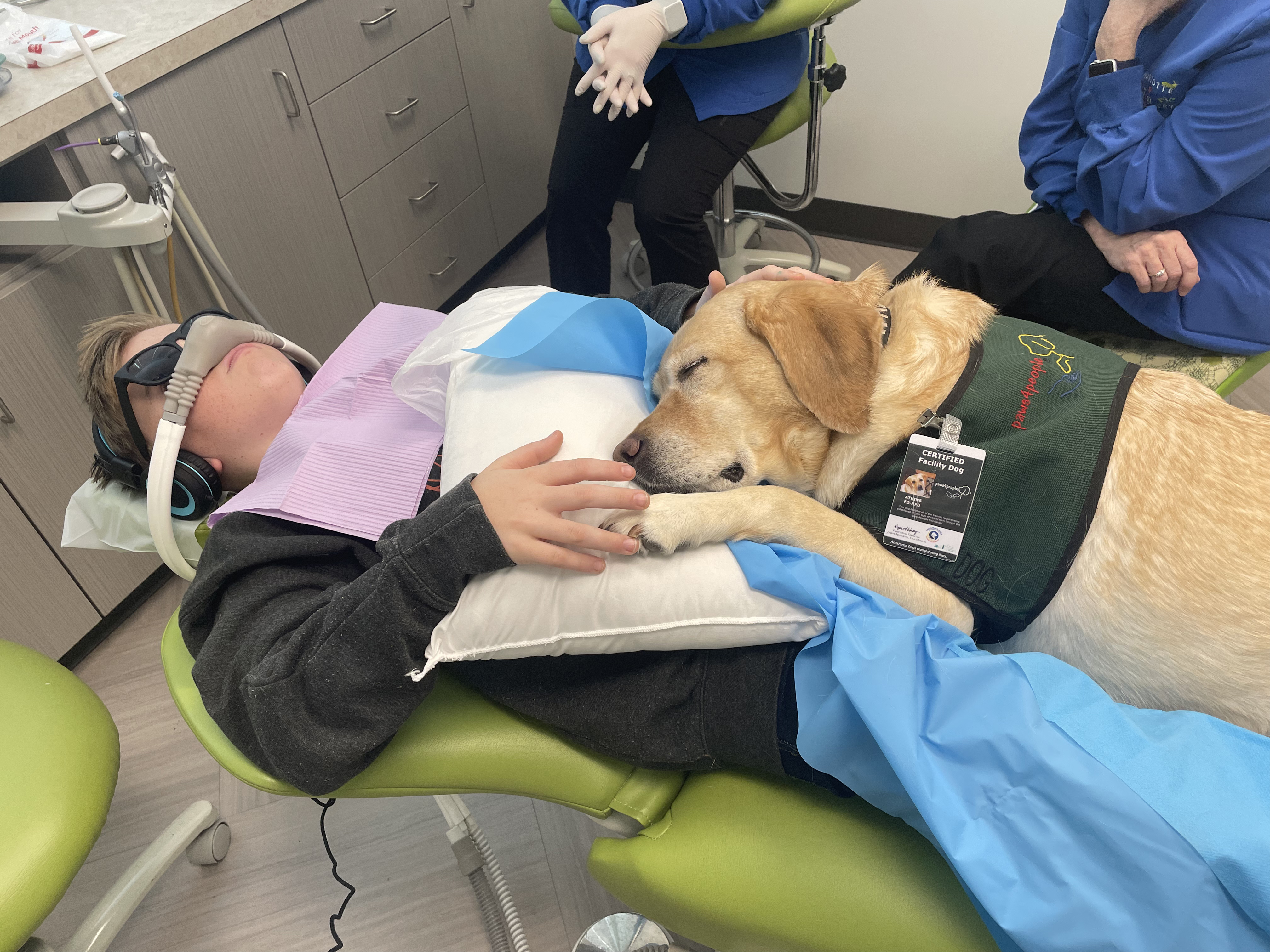 Levi McAllister lies in a dental chair with a dog sitting on his lap.