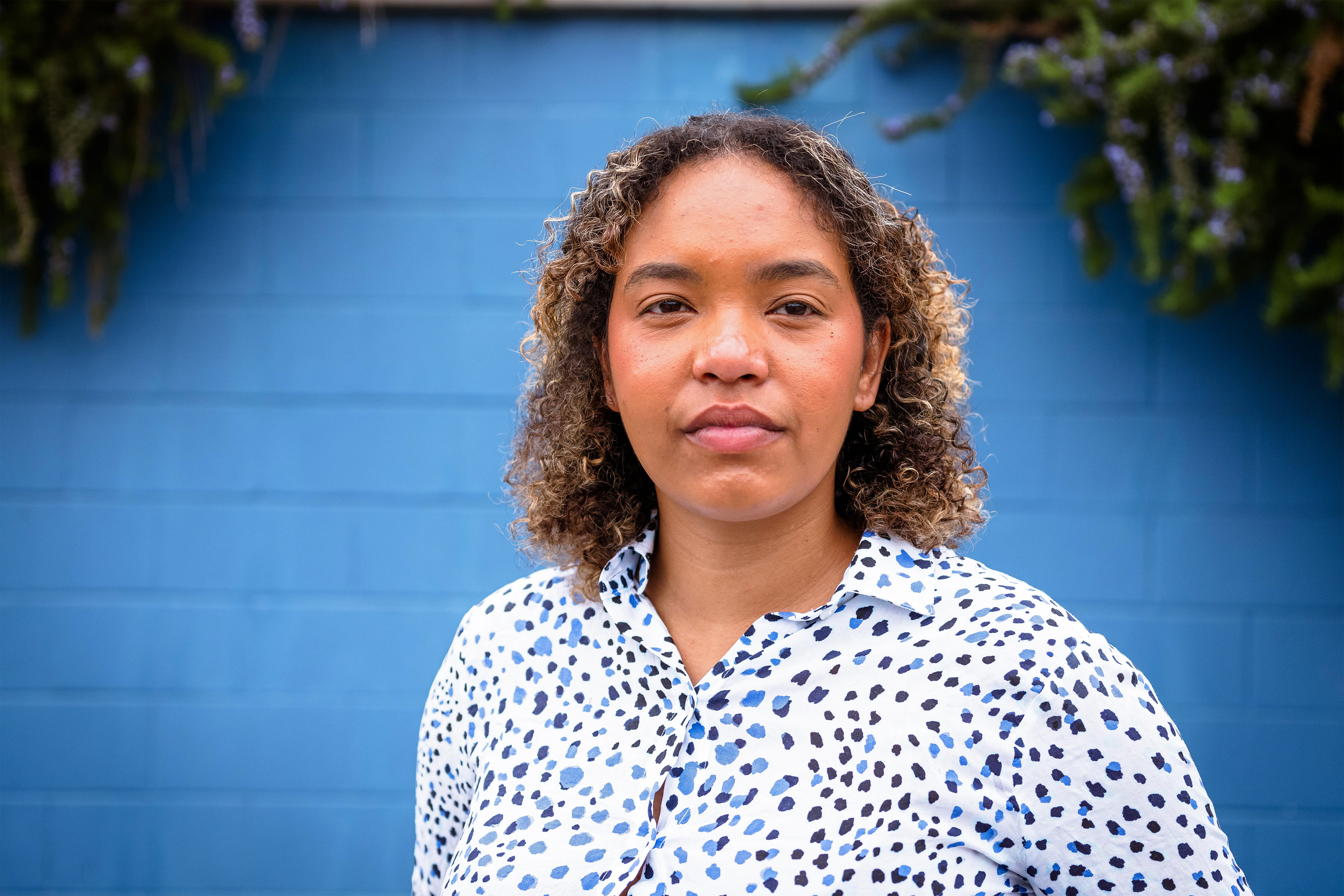 Daisha Williams stands in front of a blue wall in North Carolina. Greenery peaks over the top of the wall.