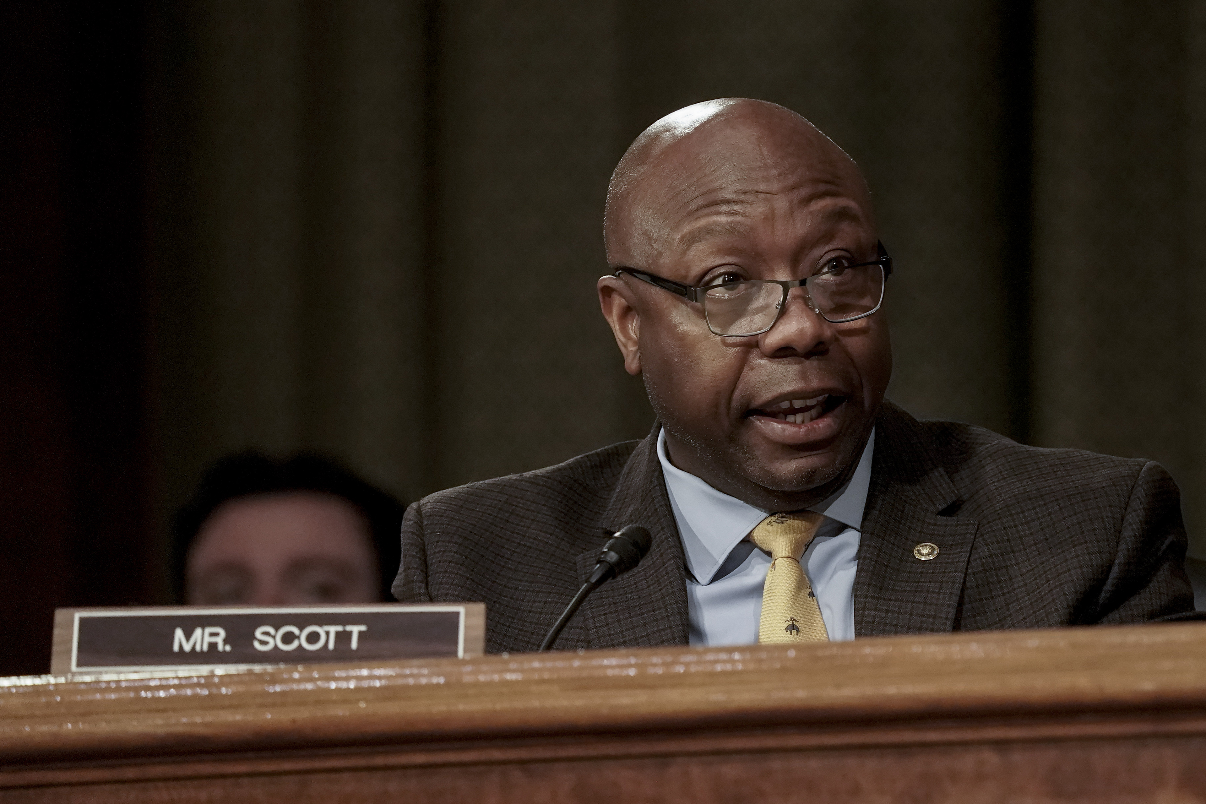 A man in a suit sitting behind a desk speaks during a Senate hearing.