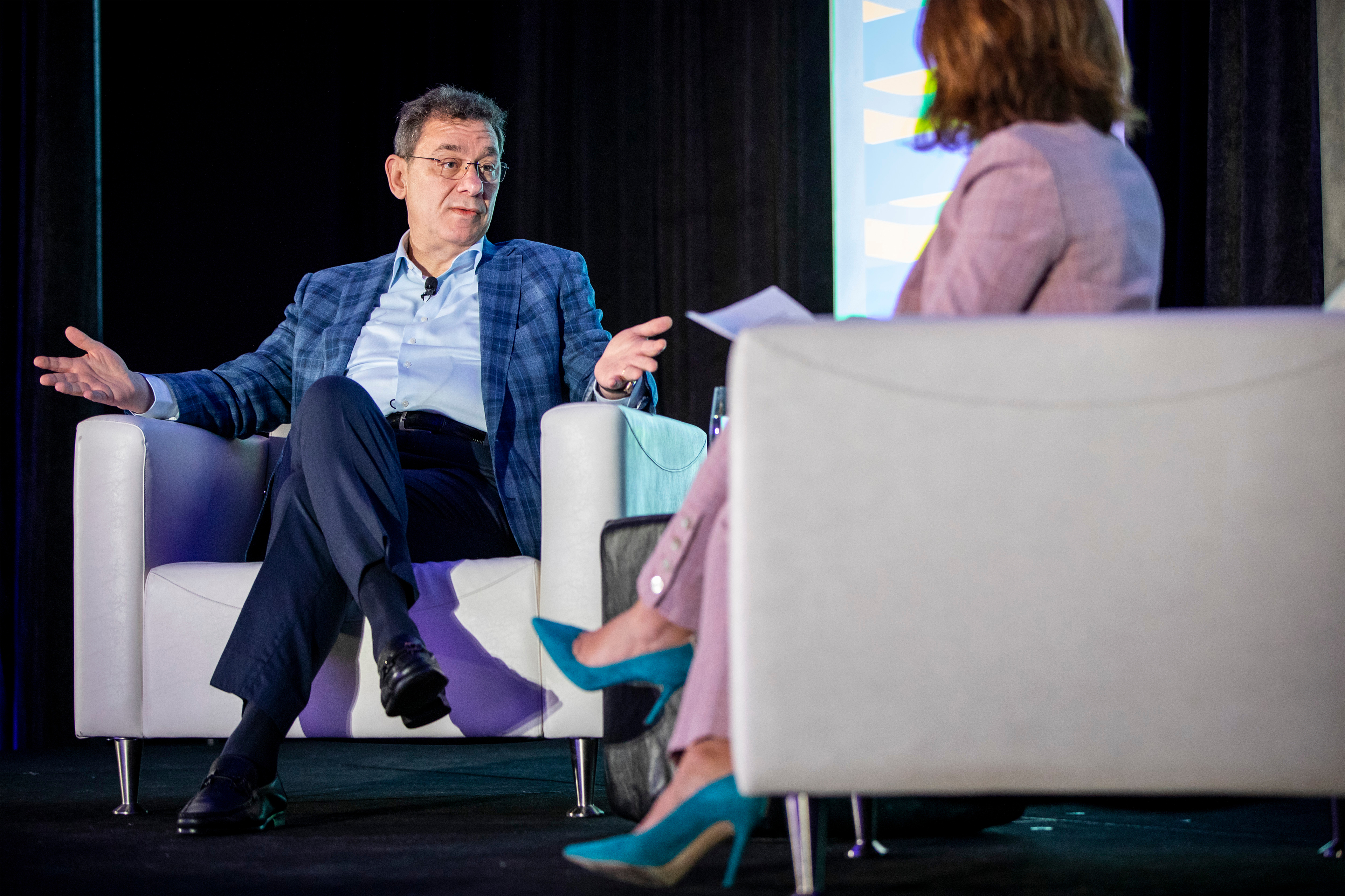 Albert Bourla is seen sitting in a chair, speaking during a panel at the South by Southwest festival. A blurred person sits on the left in the foreground.