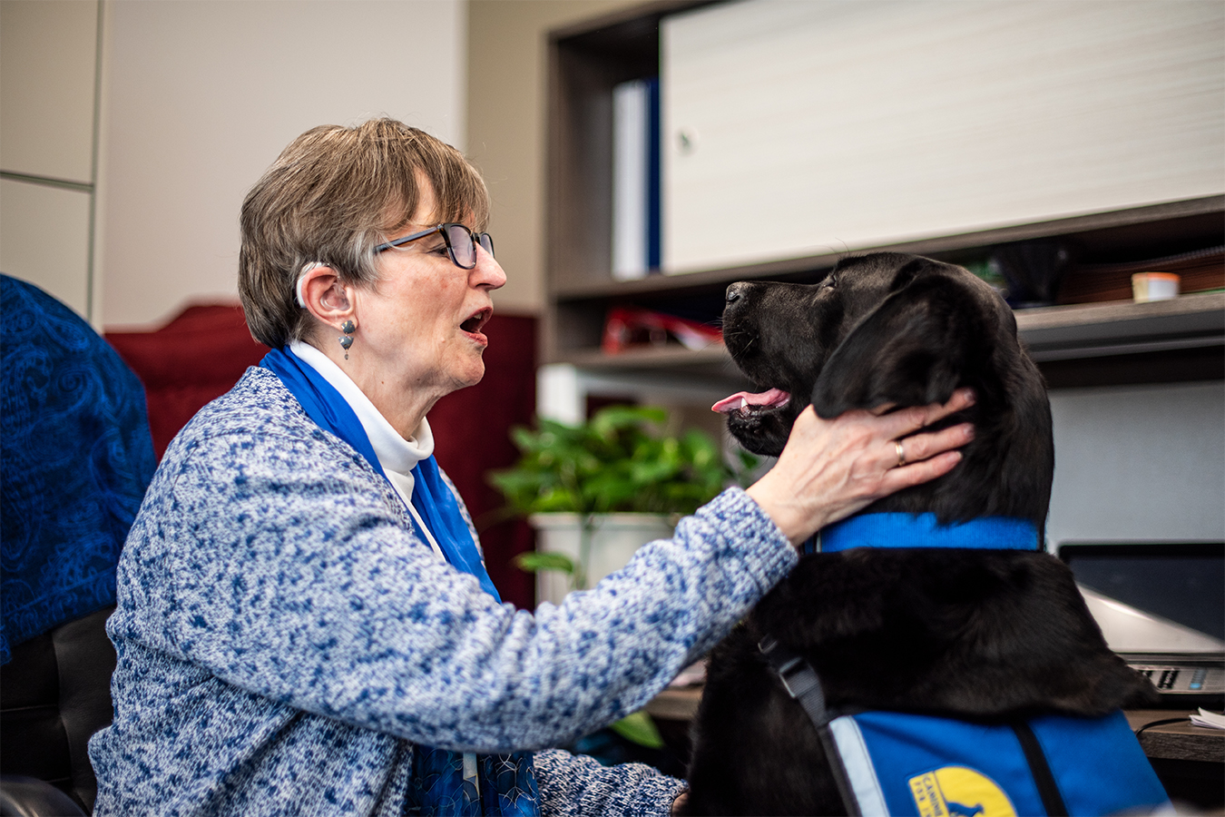 Lise Hamlin sits in an office chair, petting her black laborador/golden retriever mix hearing dog, Shine.