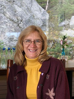 Laurie Scherrer smiles in front of a grassy backdrop.