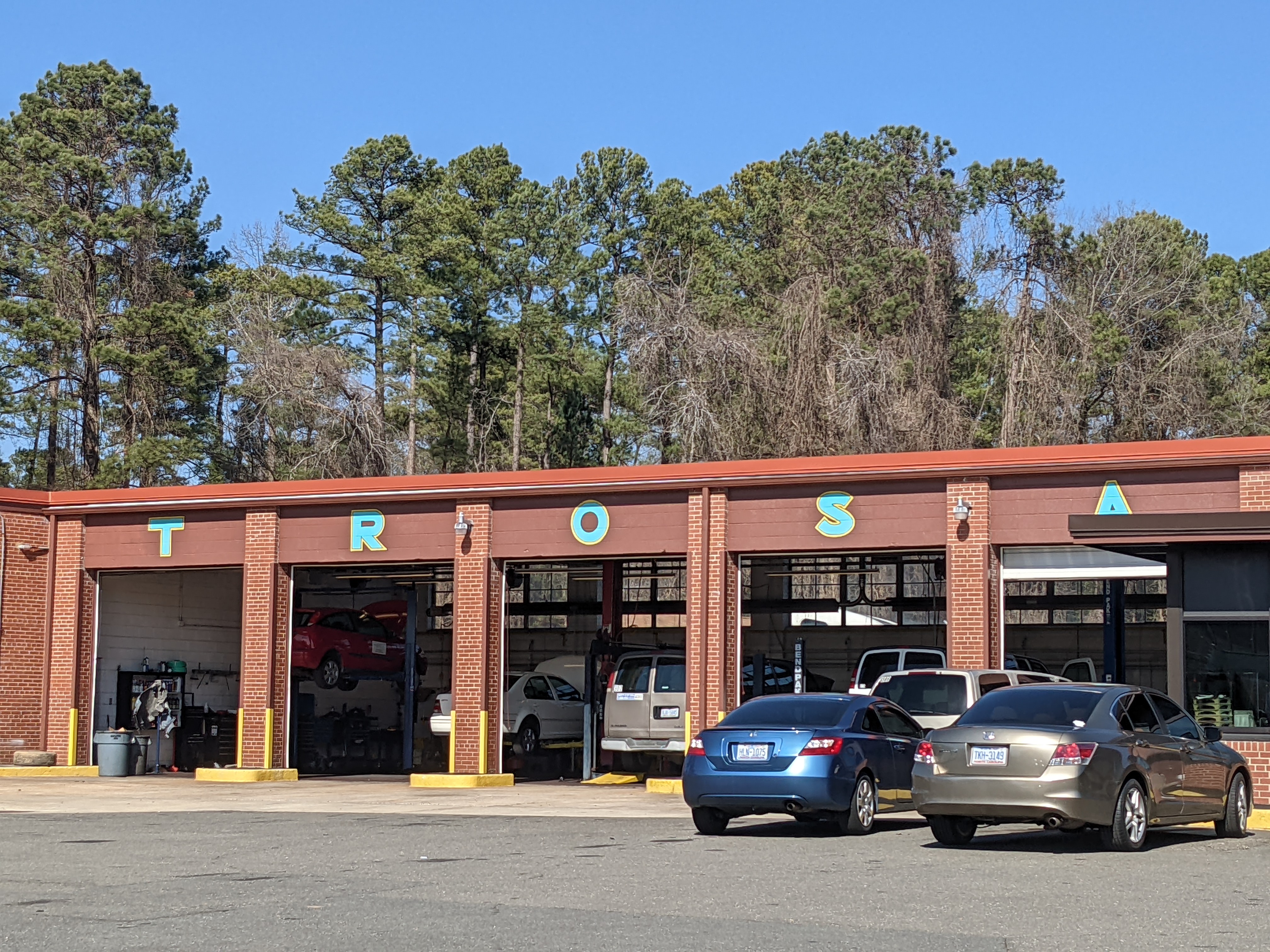 cars lined up inside and outside a brown body shop with the word TROSA painted in teal over each garage