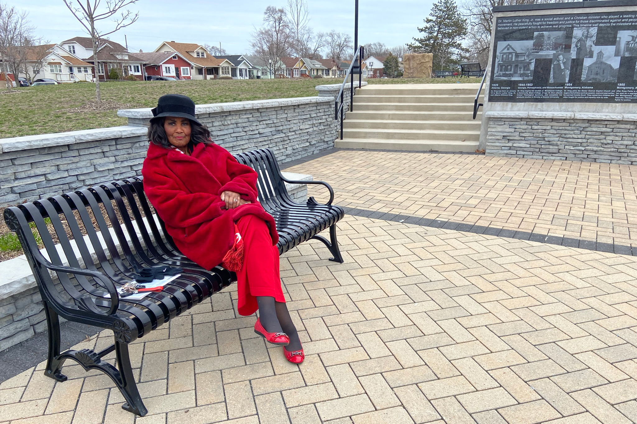 Carlotta Blake-King is seen sitting on a park bench. Her hands are folded in her lap.