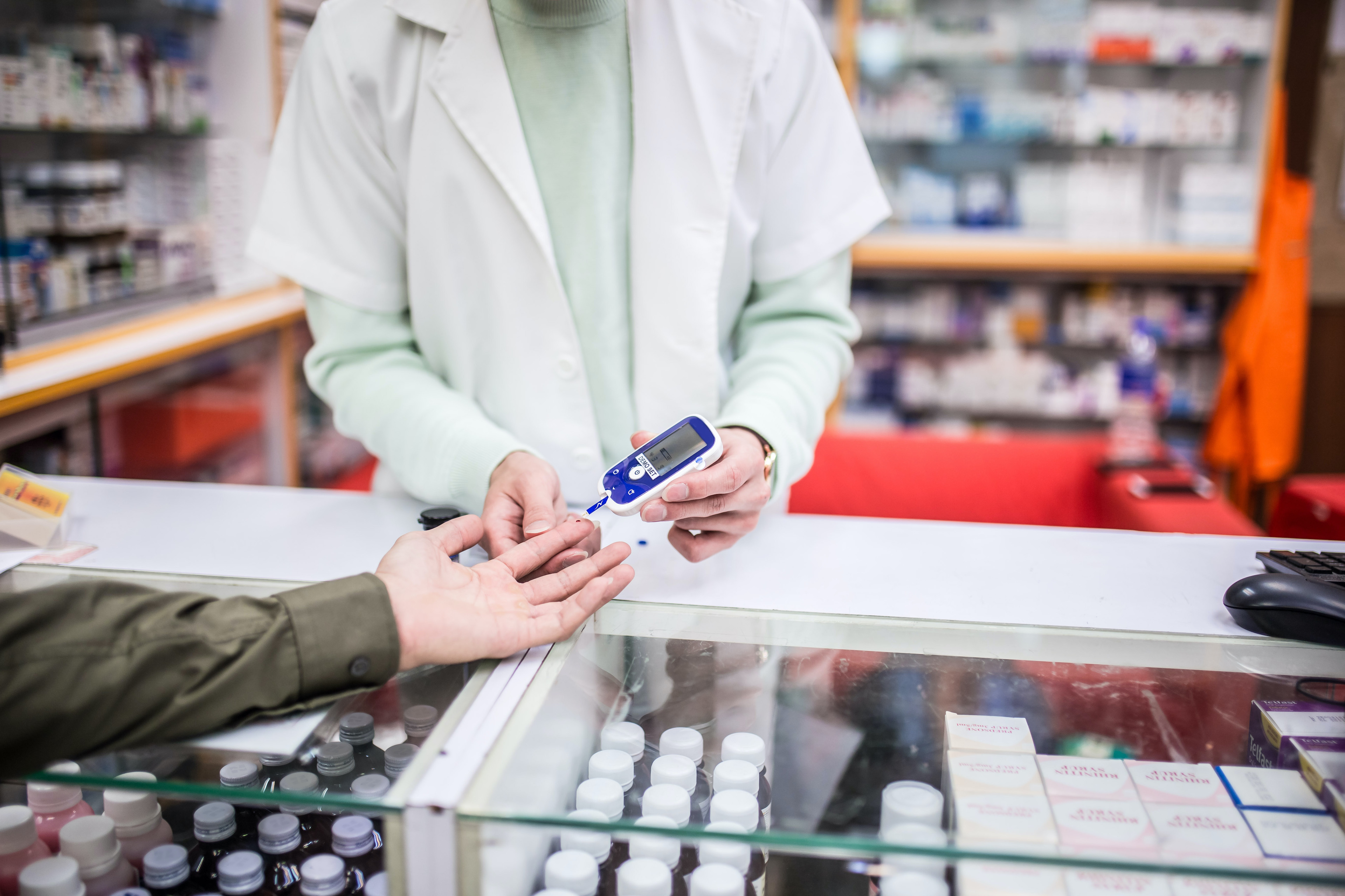 An Asian Chinese male pharmacist helping customer doing blood sugar test at pharmacy counter. Close up shoot sugar test.