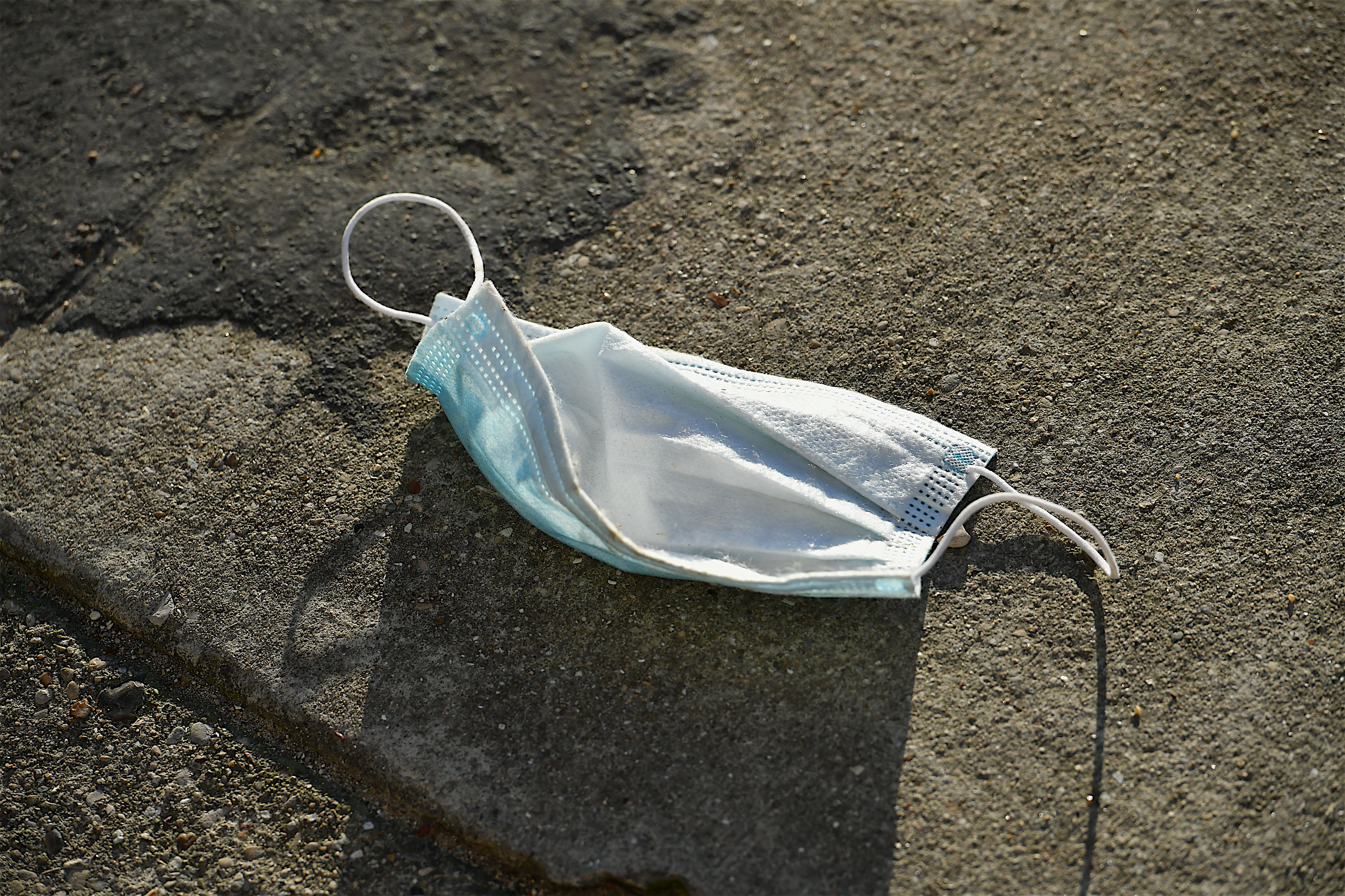 A discarded surgical face mask lies on pavement.