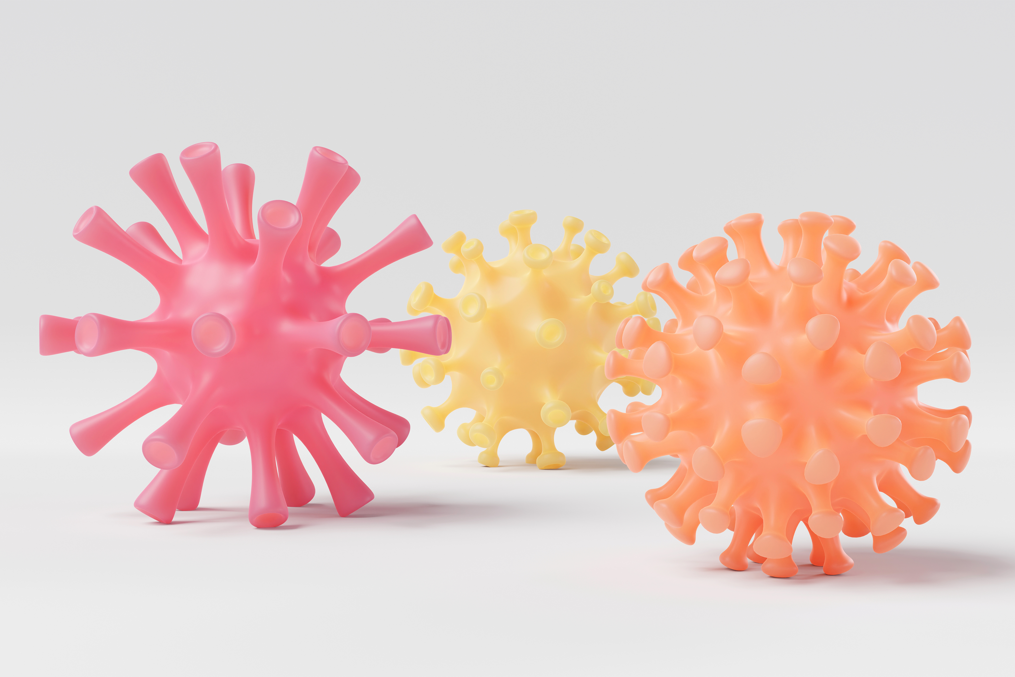 A 3D rendering shows three models of the coronavirus tinted pink, yellow and orange on a white background.