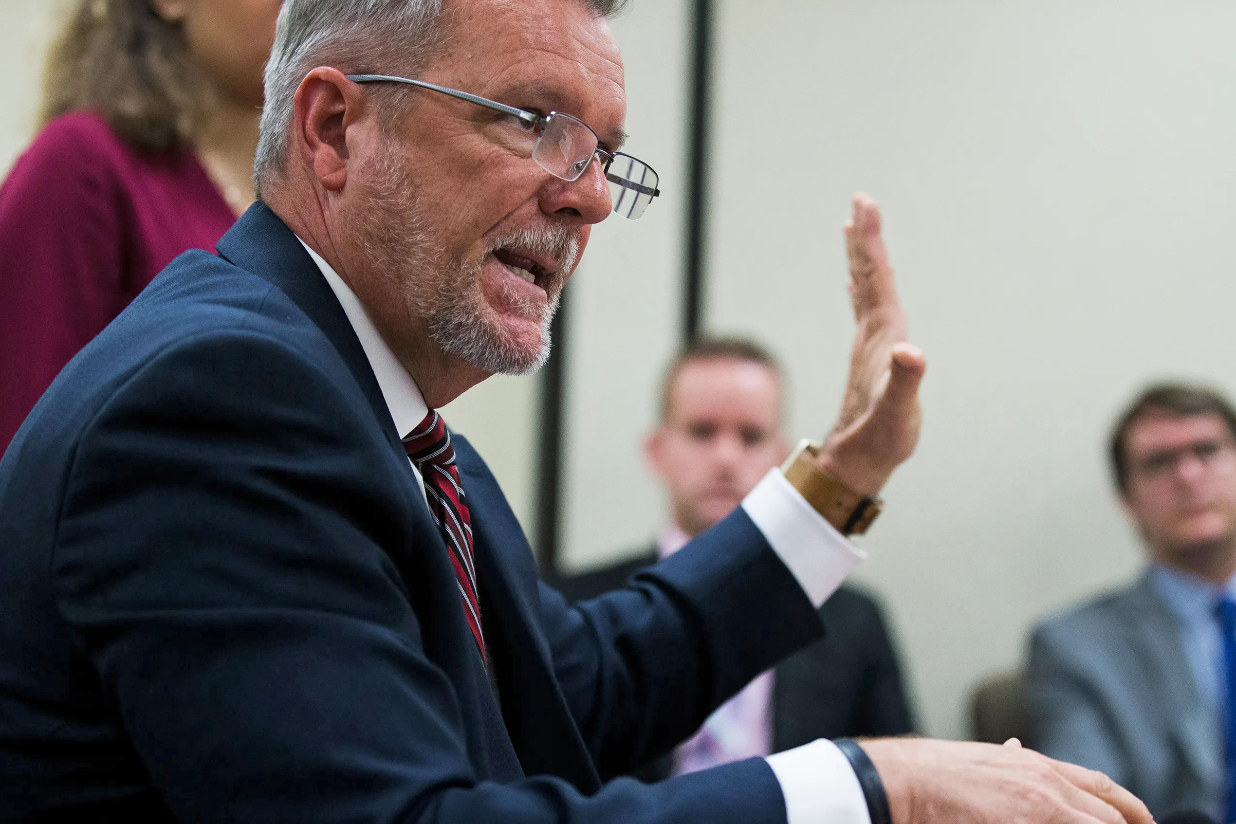 Mike Randol is seen in this photo from the side. He is speaking before the Iowa Council on Human Services and raising his left hand.