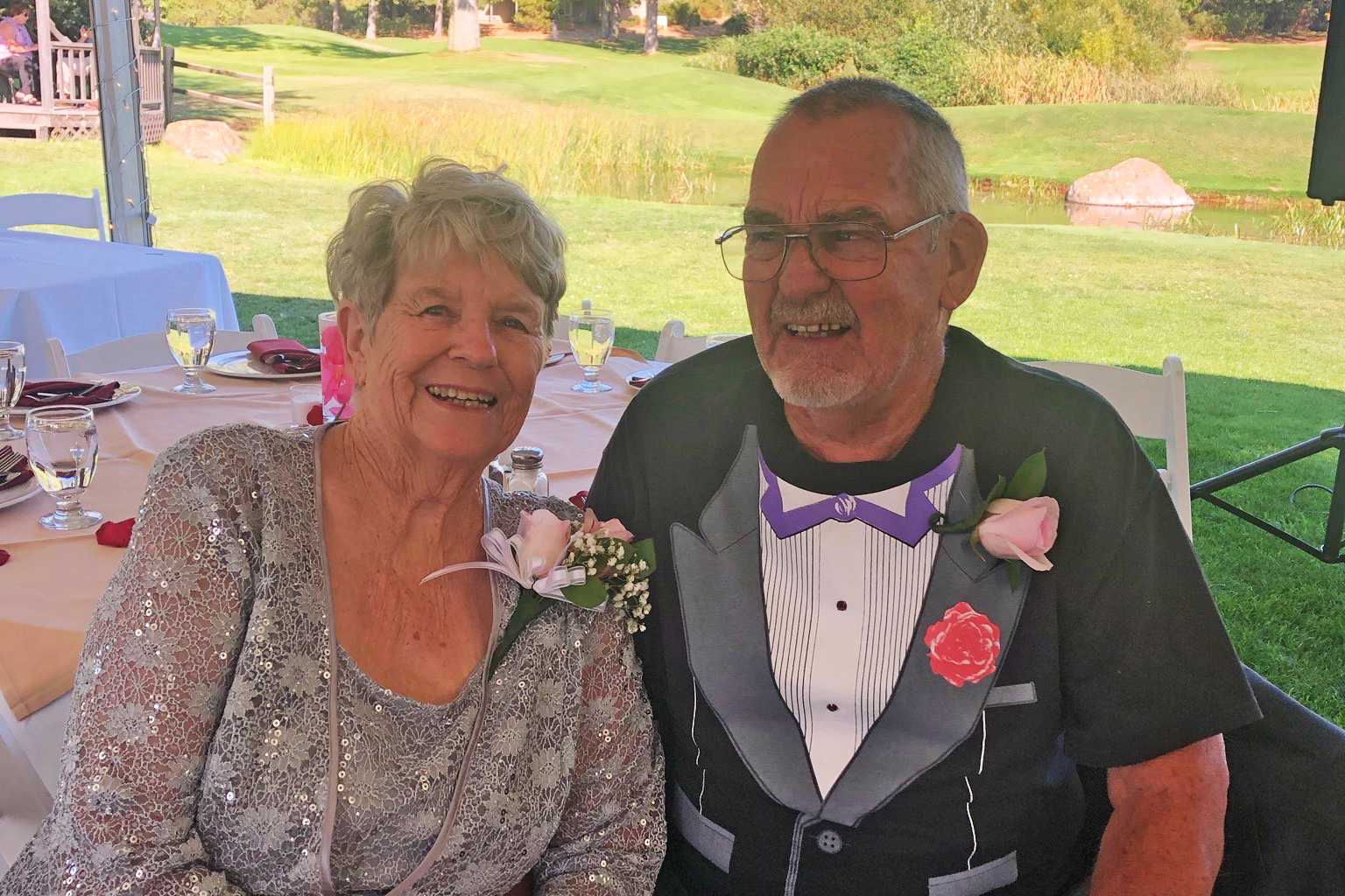 Johanna and Trenerry are seen sitting next to one another in front of a table, posing for a photo together. The two are dressed for a wedding.