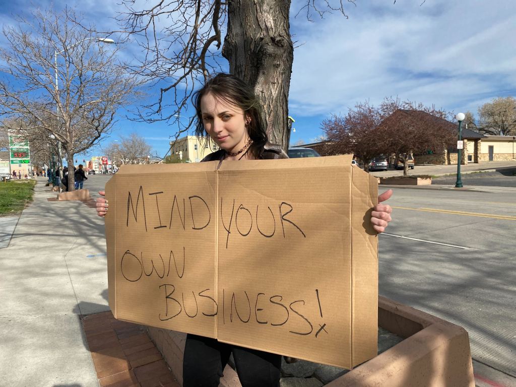 A young woman holds a sign that reads, "Mind Your Own Business!"
