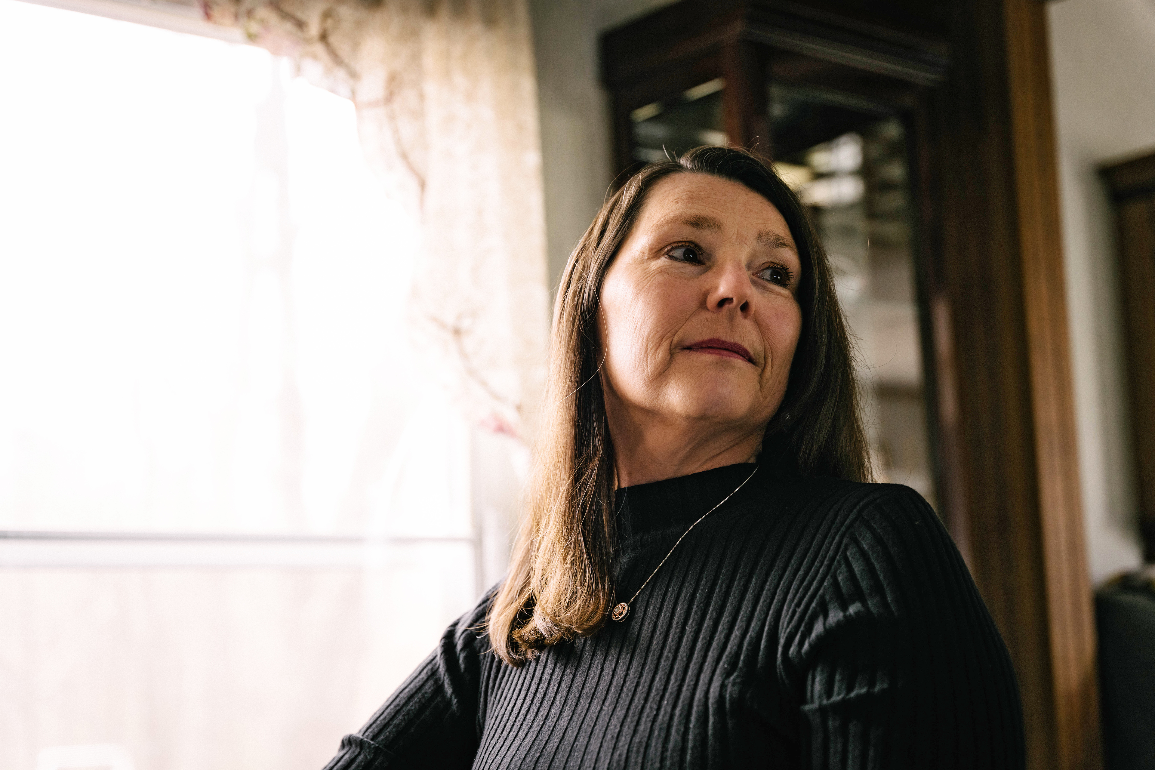 Dee Tate is seen posing for a portrait, sitting beside a window, looking to the right.