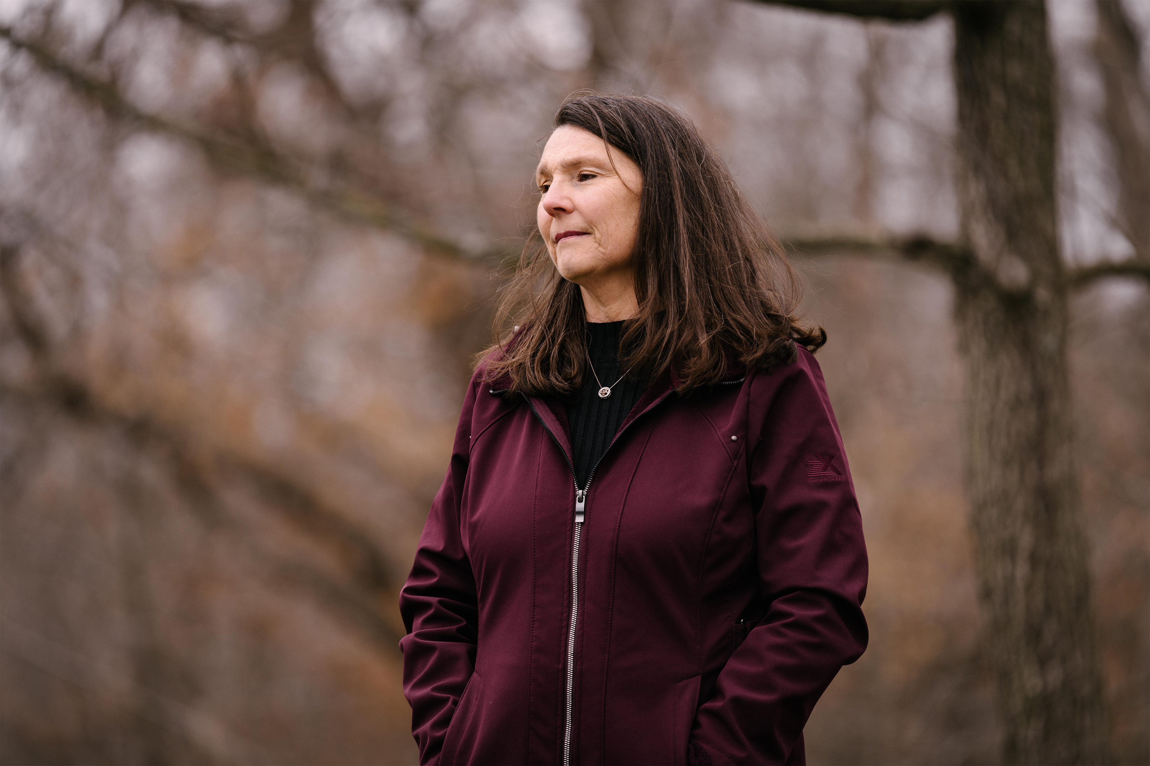 Dee Tate poses for a portrait outside with trees blurred in the background behind her.