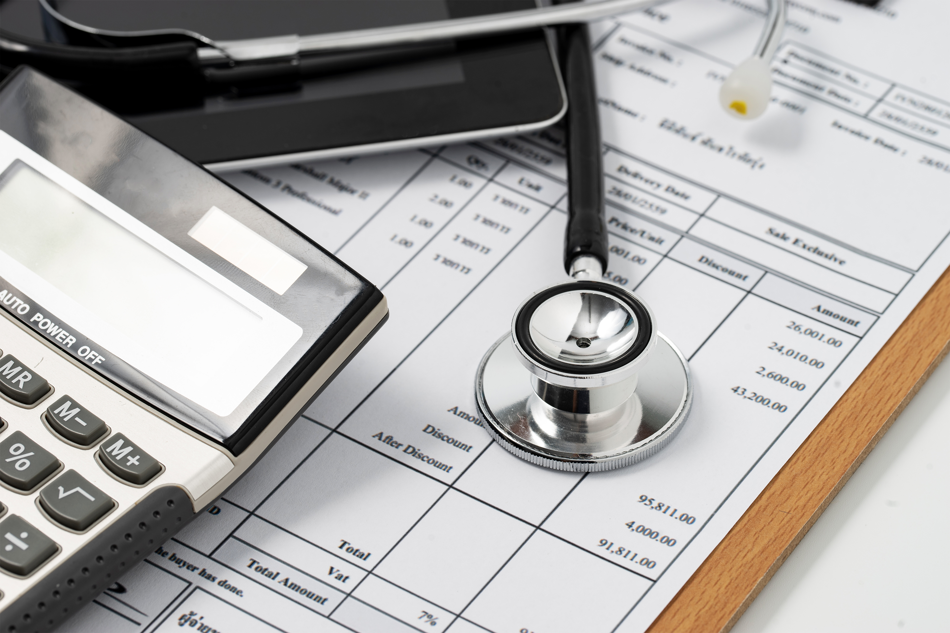 A clipboard with a medical bill is seen. A stethoscope and calculator lay on top of it.