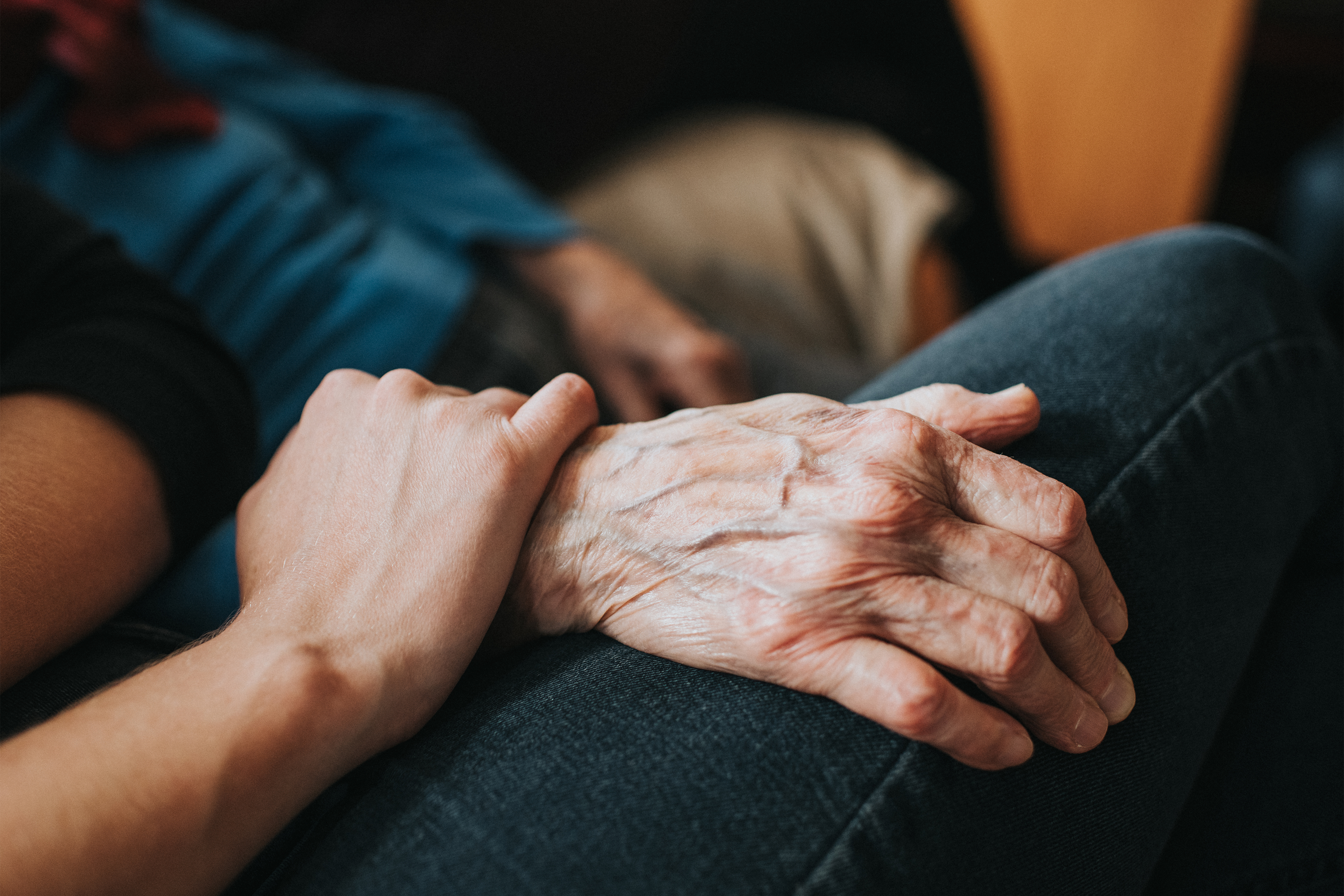 A closeup photo shows a younger person holding an elderly person's wrist.