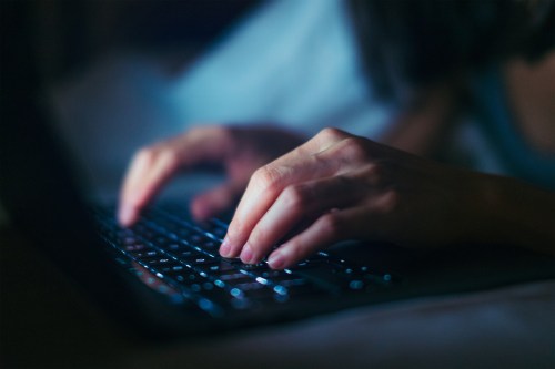 A close-up photo shows hands typing on a laptop keyboard in the dark.