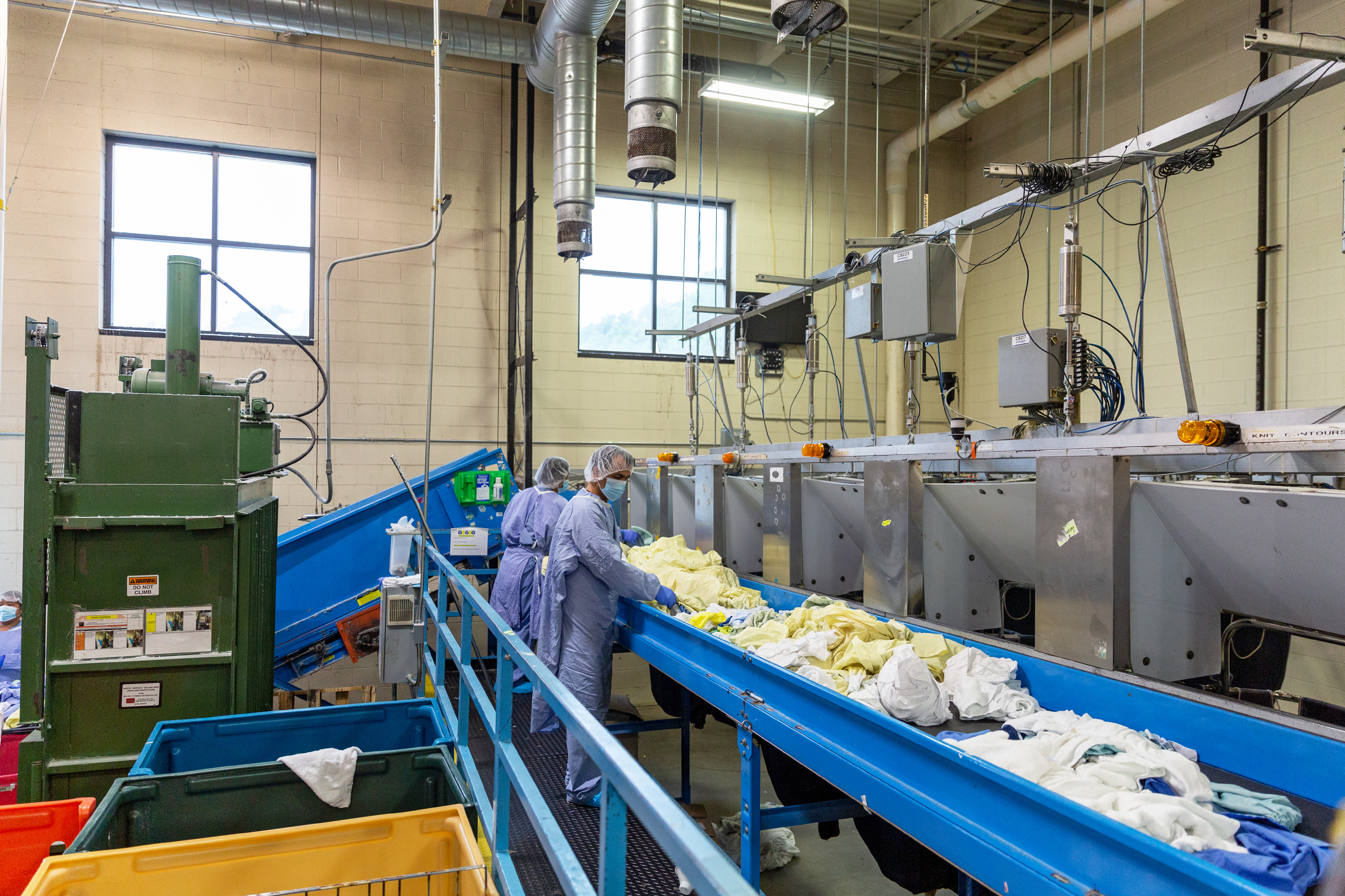 A photo shows laundry workers placing isolation gowns and linens on a conveyor belt.