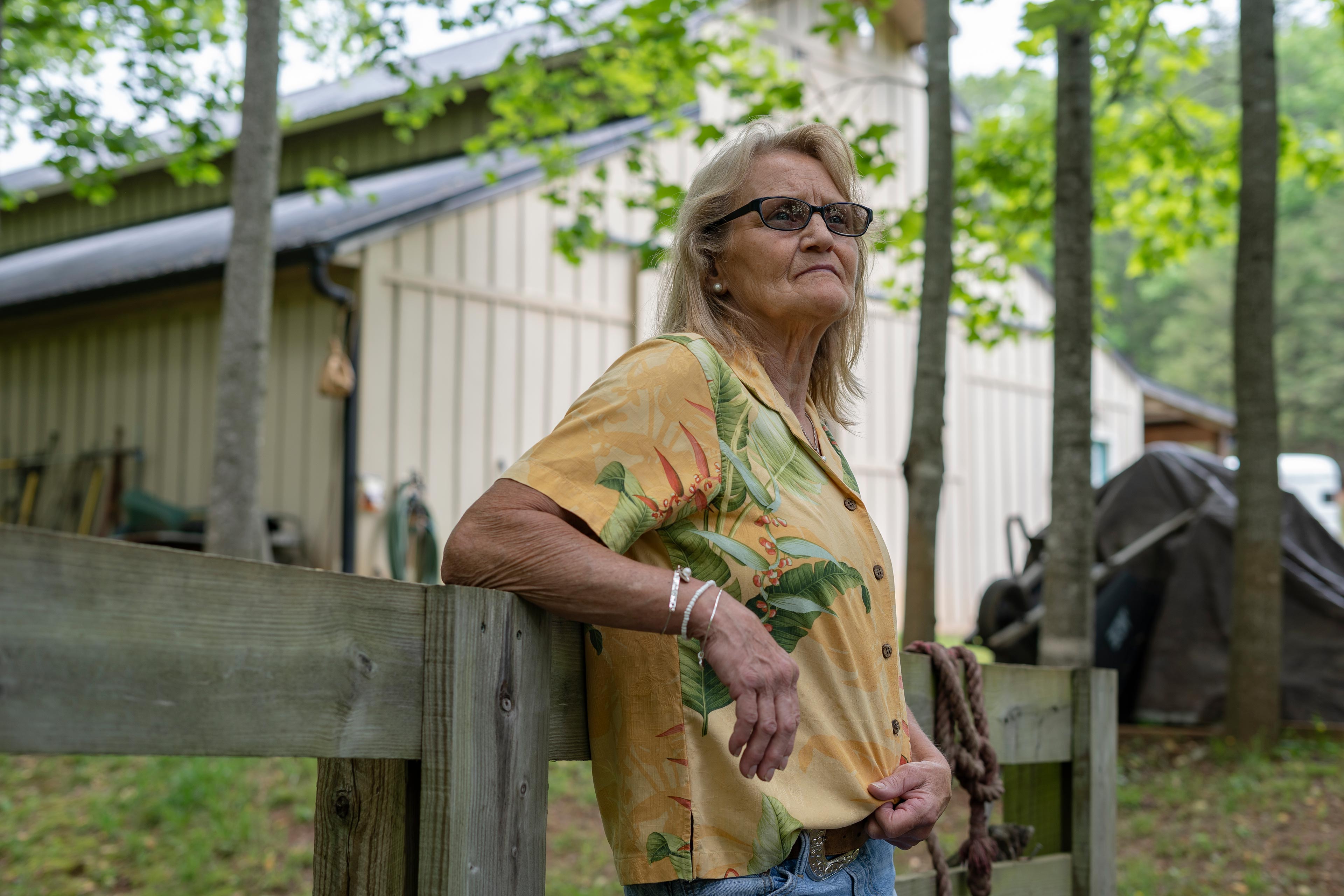 A woman leans against a wooden fence.