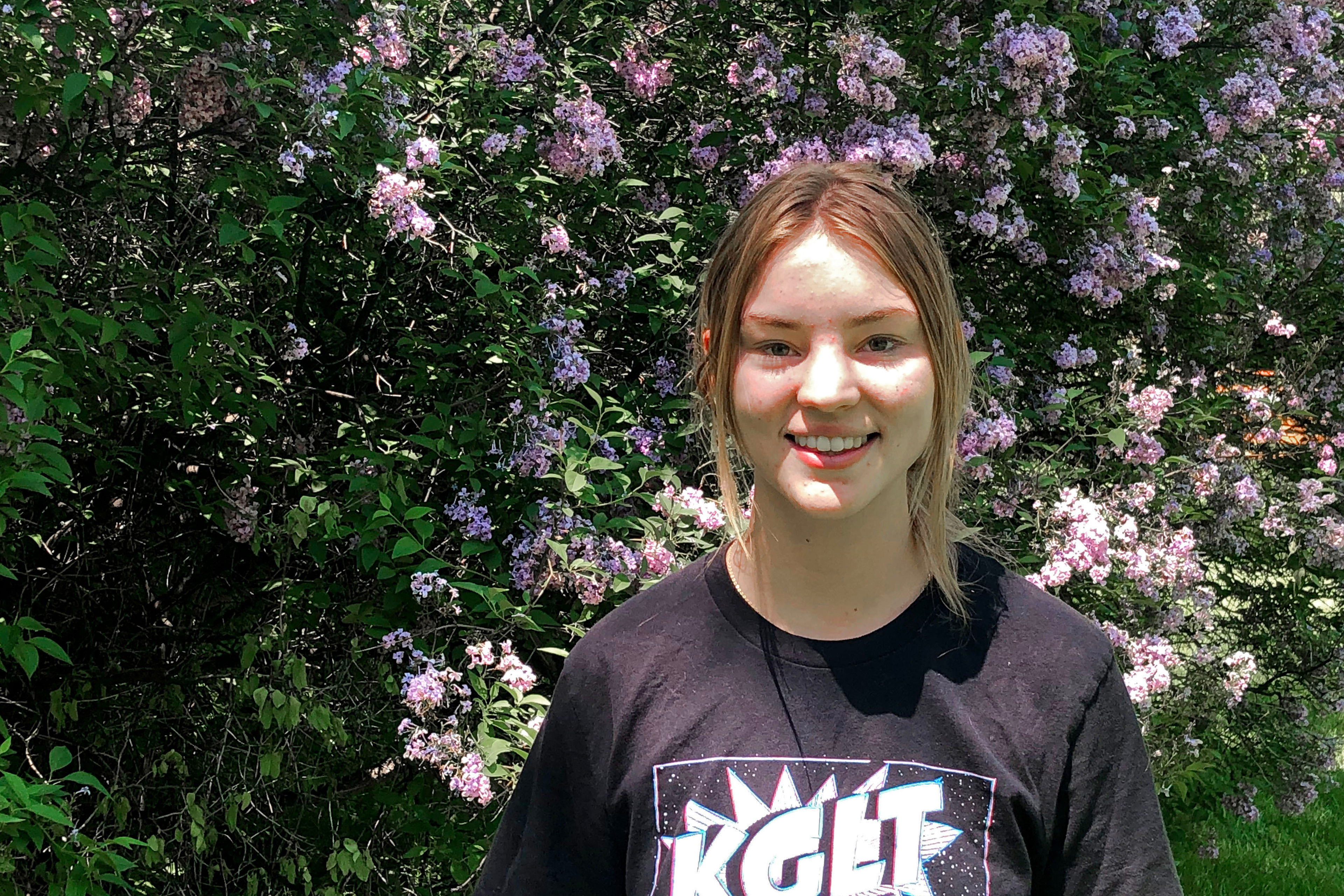 A photo shows Claire Vlases standing outside by a flowering shrub.