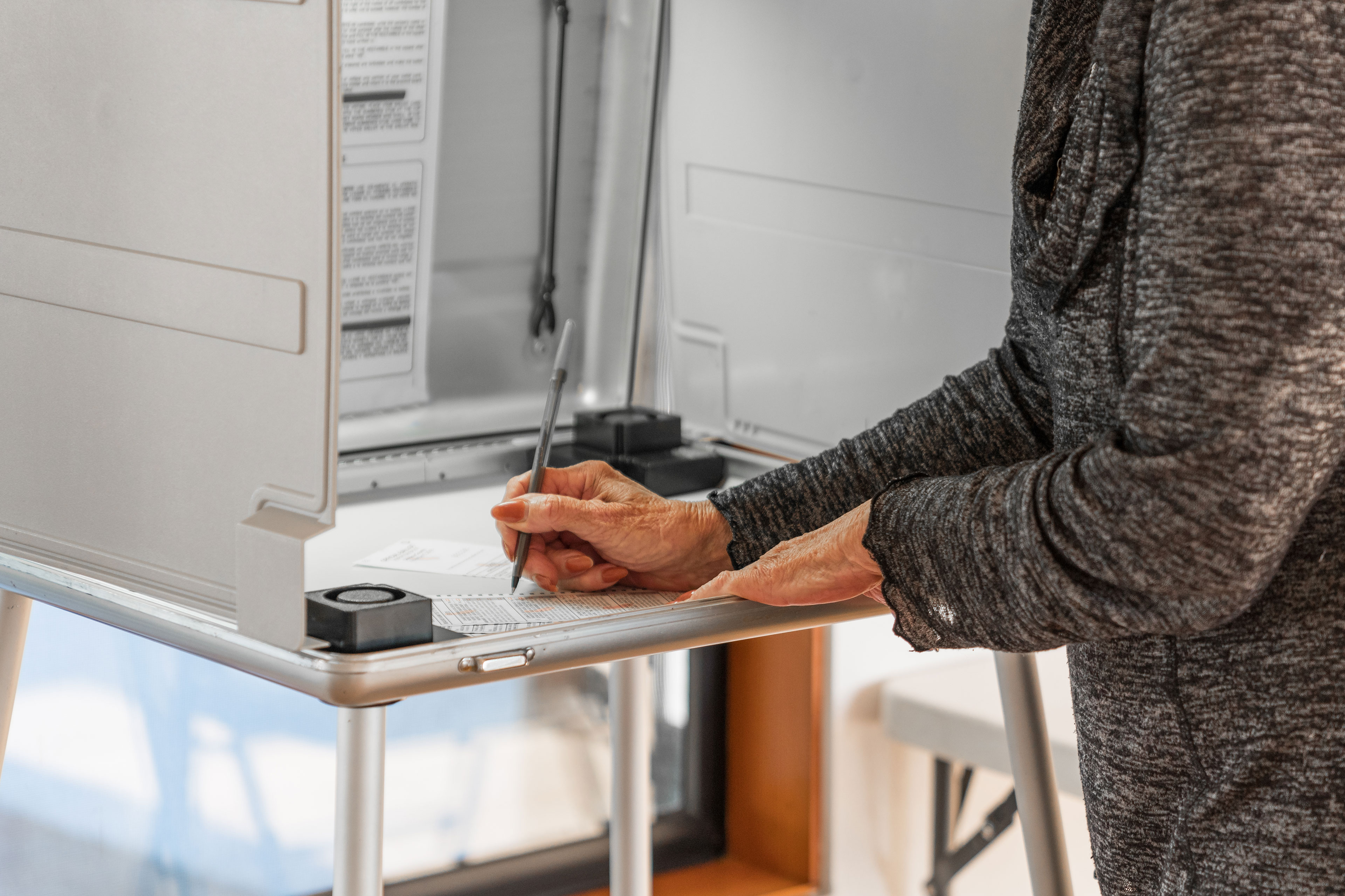 A woman standing at a voting booth marks a ballot.