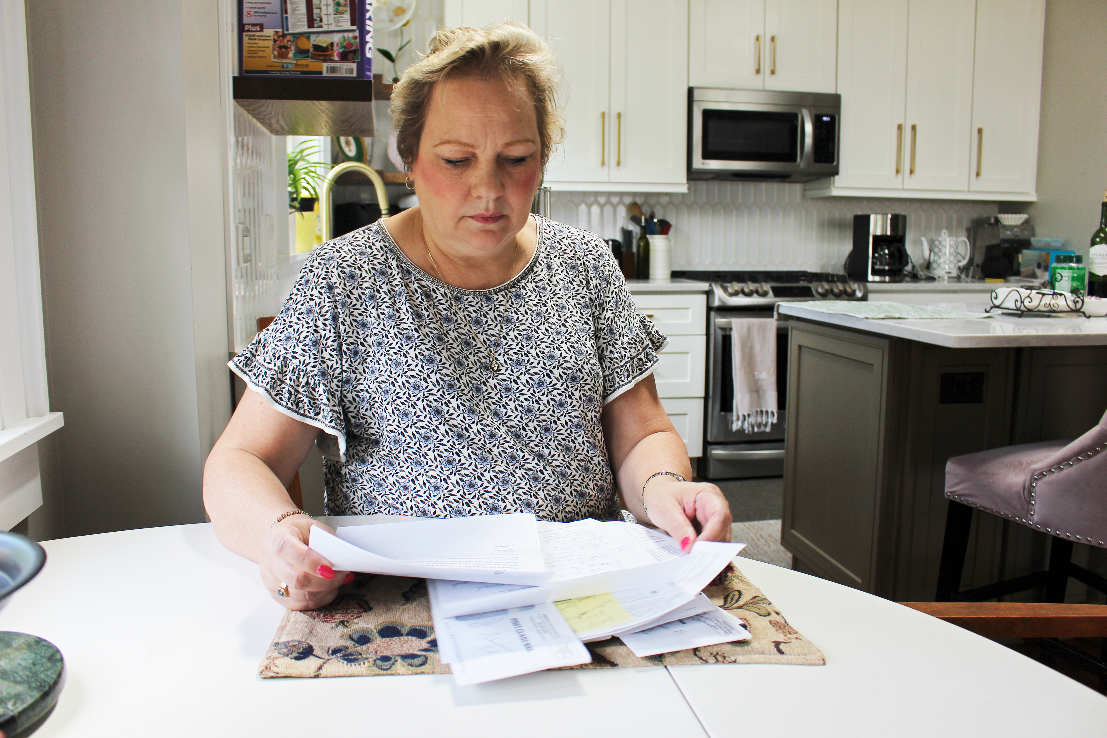 A photo shows Peggy Dula in her kitchen looking at her medical bills.