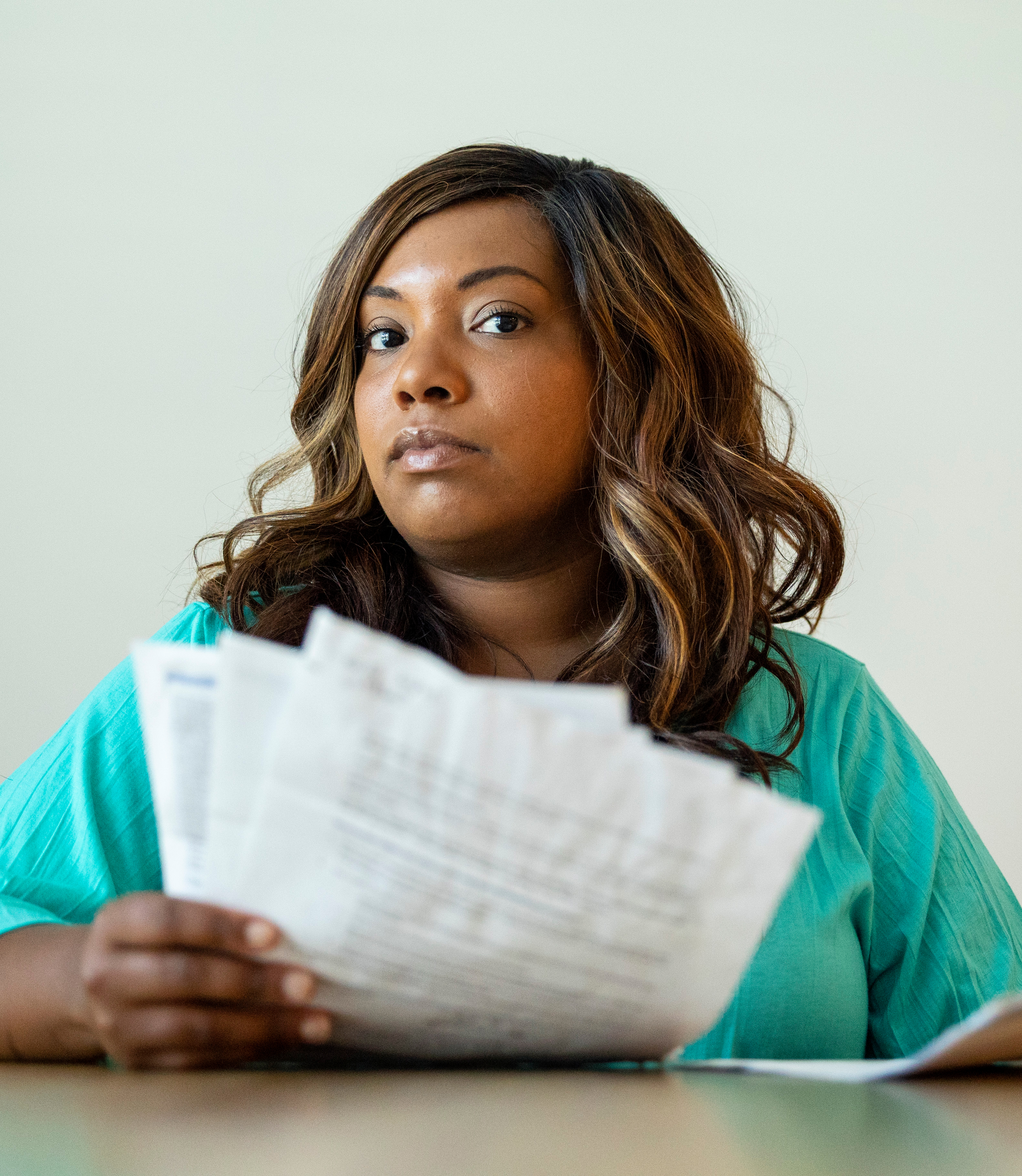 A photo shows Dani Yuengling sitting at a table while holding a stack of her medical bills.