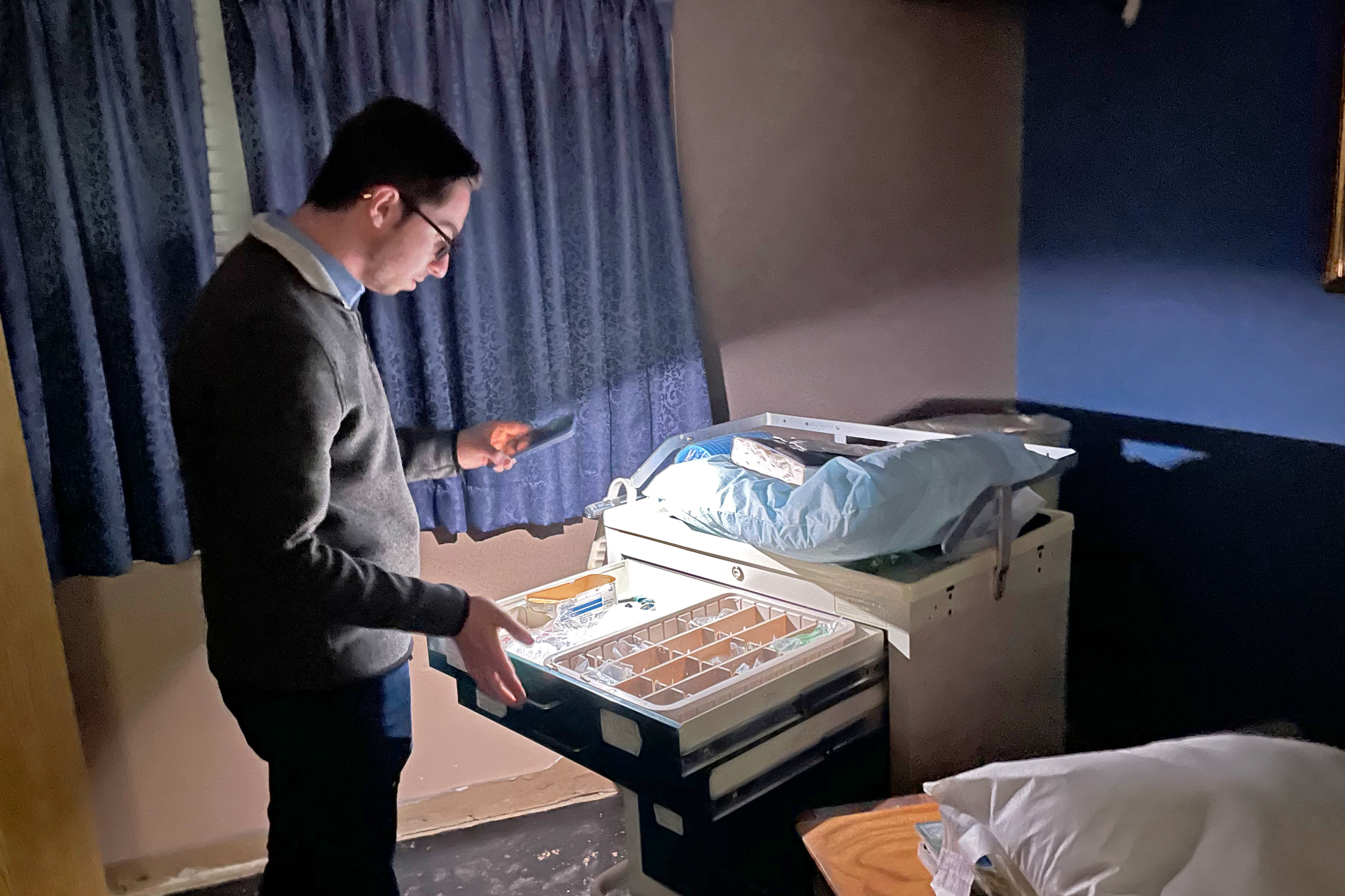 A photo shows Kyle Kopec using his phone as a flashlight to look through an old supply cabinet.
