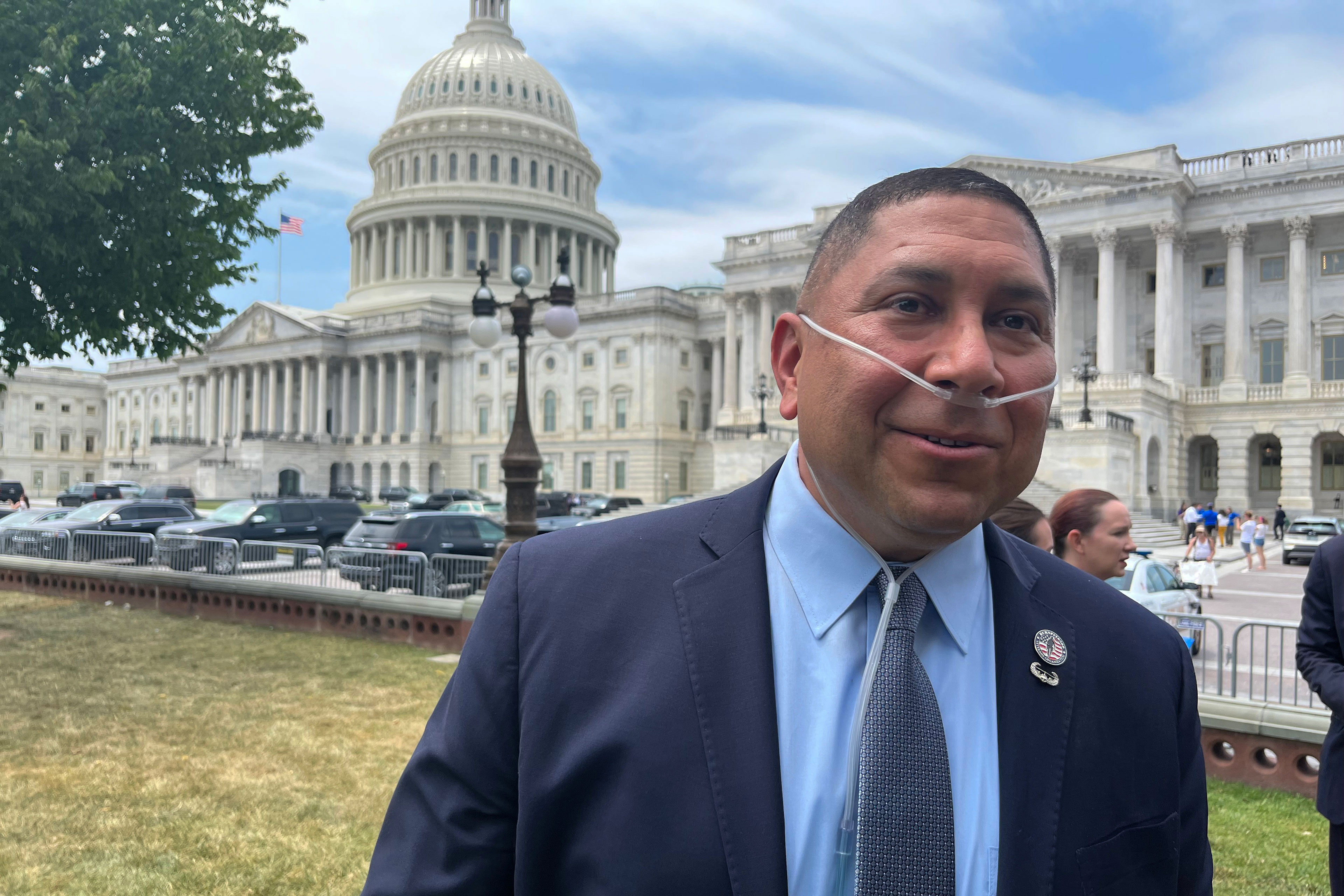 A man in a suit and wearing a nasal cannula stands on the north side of the Capitol building.