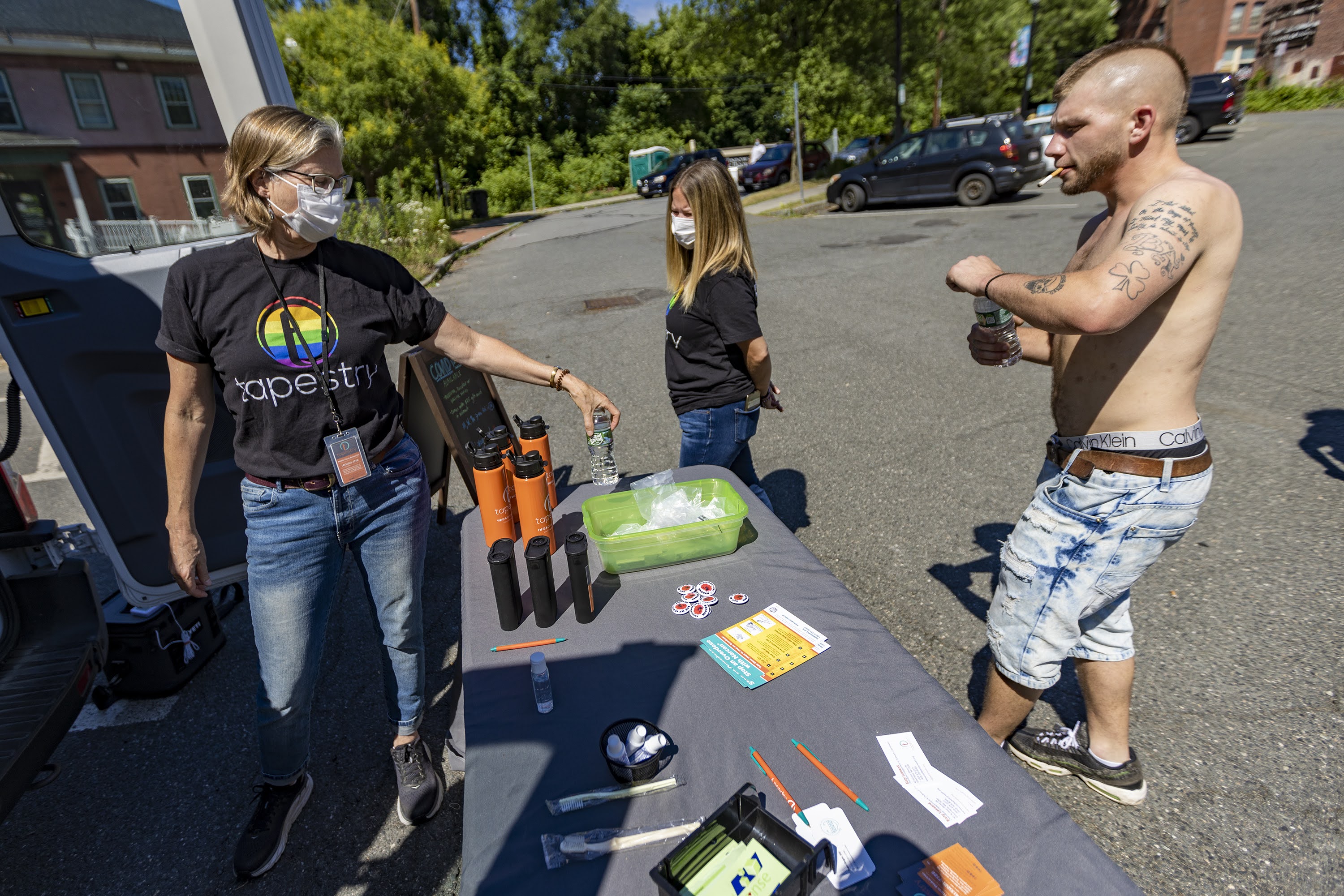 A photo shows Kyle approaching a pop-up harm reduction unit table.