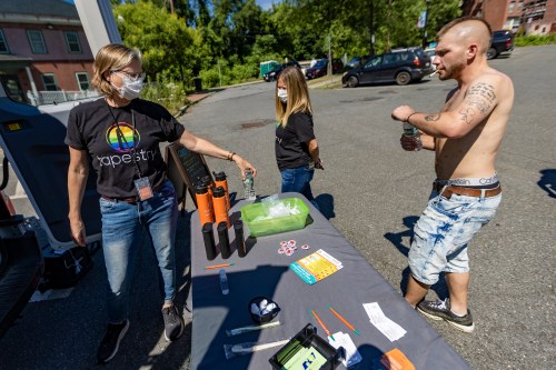 A photo shows Kyle approaching a pop-up harm reduction unit table.