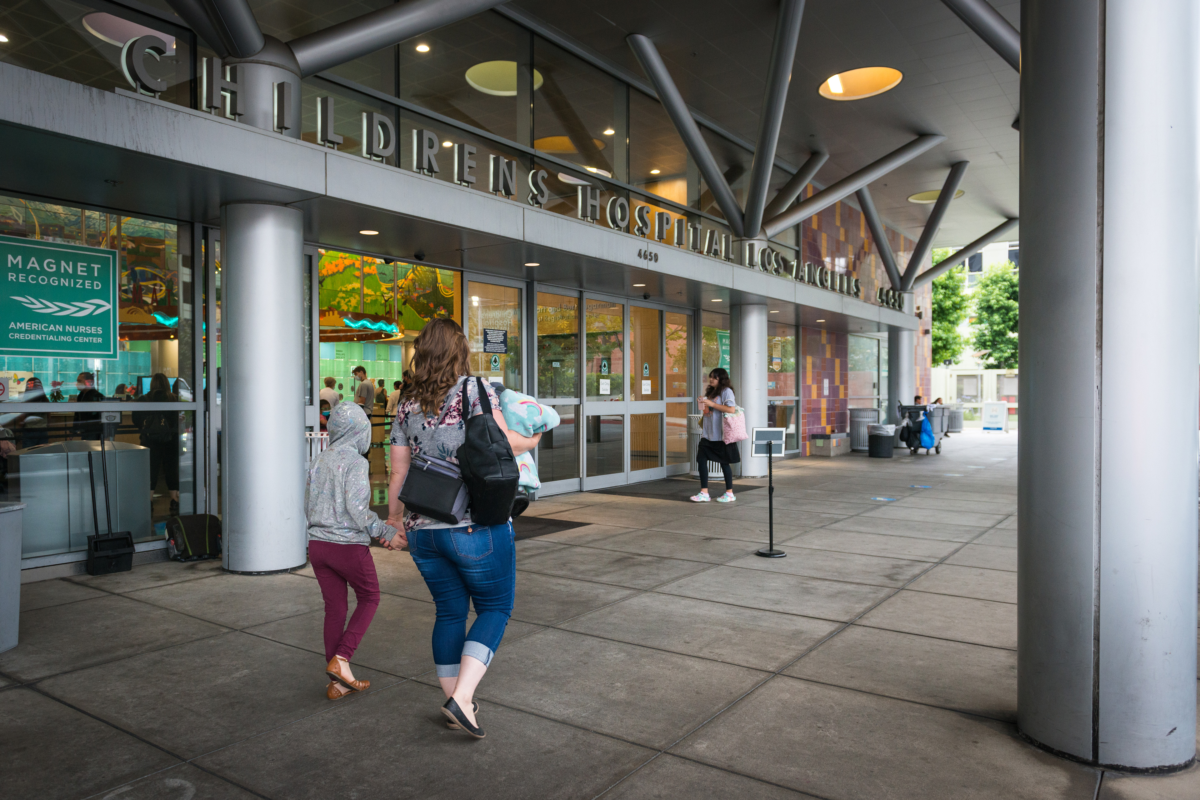 Deborah and her daughter, Annabelle Lewis, walk towards the glass entrance doors to a Children's Hospital.