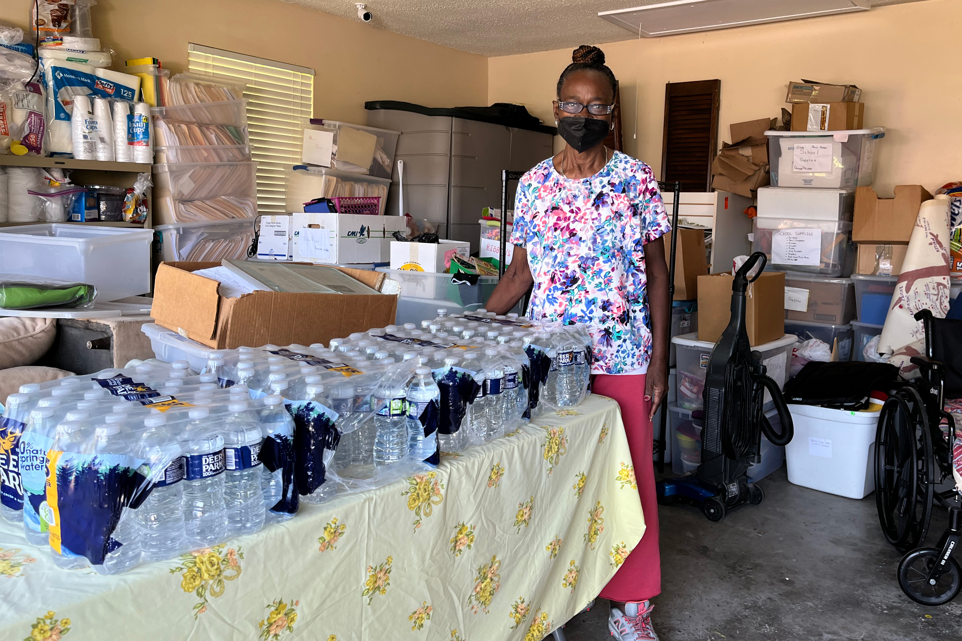 A photo shows Thelma Kinney Cornelius in her garage next to a table filled with water bottles.