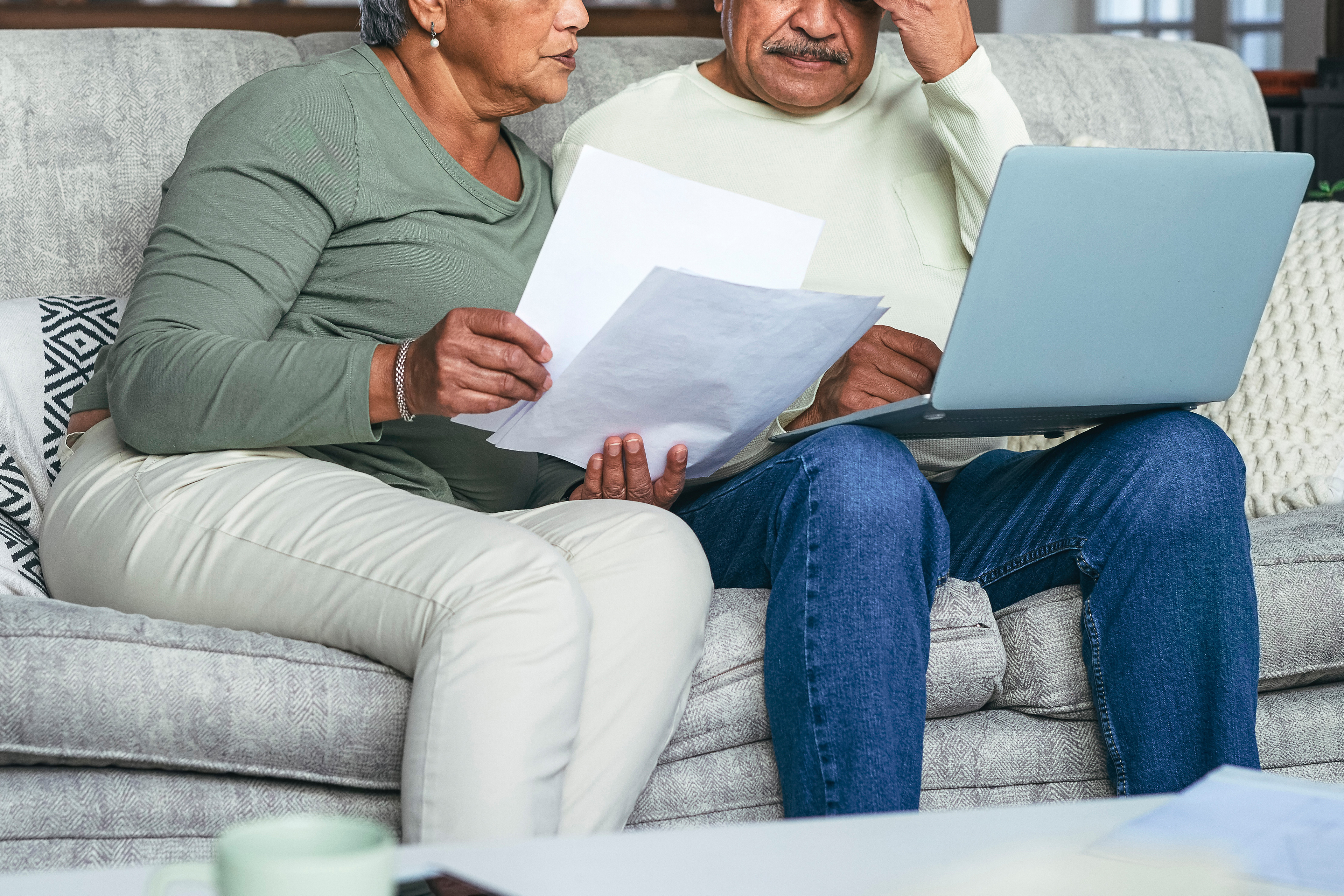 A photo shows an elderly couple sitting on a couch and looking over paperwork and a laptop together.