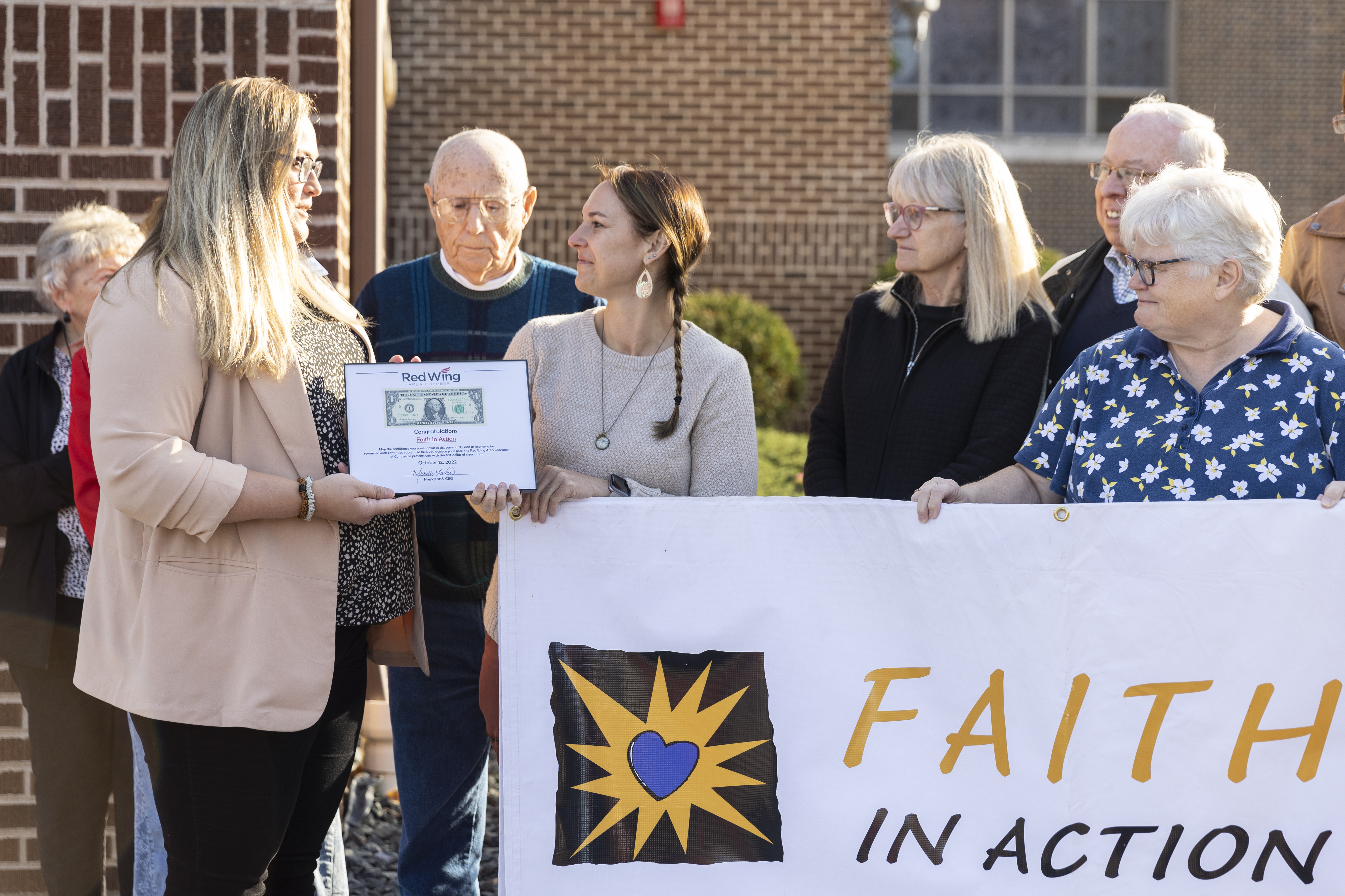 A photo shows Michelle Larson handing a certificate to Katherine Bonine at a ribbon-cutting ceremony.