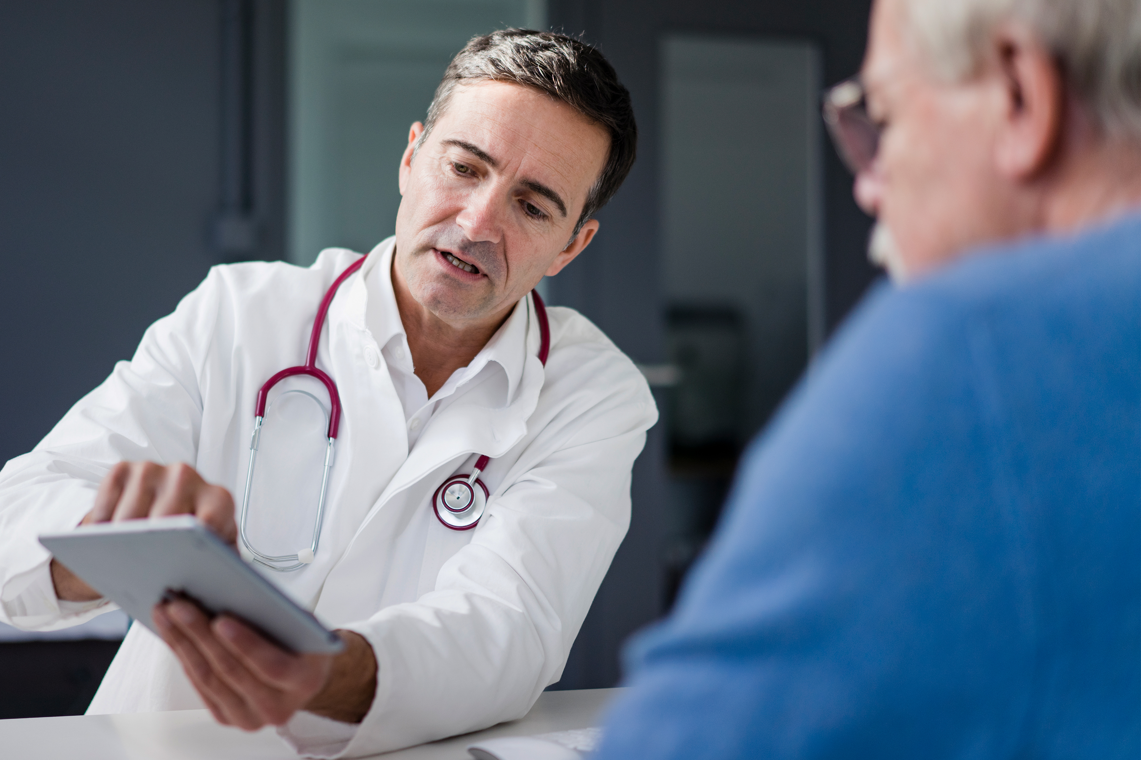 A photo shows a doctor showing an elderly patient with glasses information on a tablet screen.