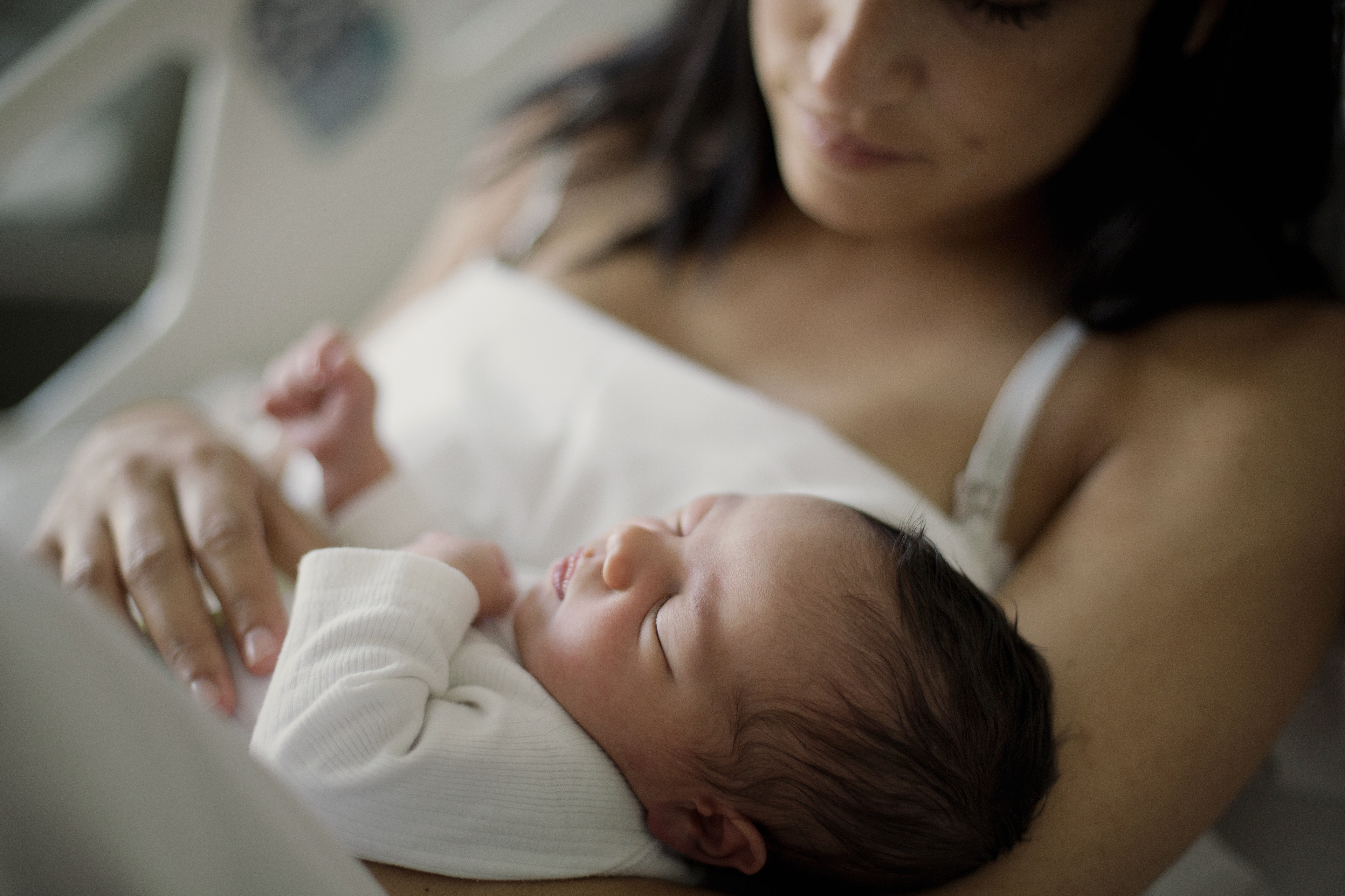 Newborn girl sleeps in her mother's arms. The mother is in a hospital bed and gown.