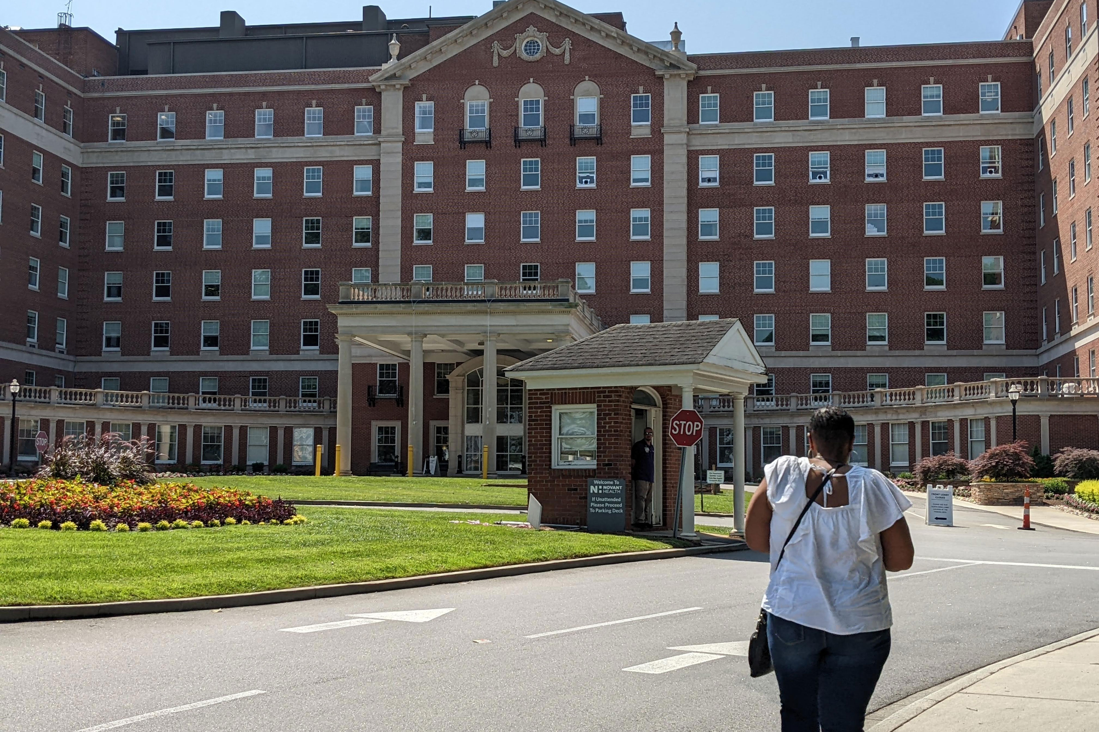 A woman walks towards a red brick hospital building.