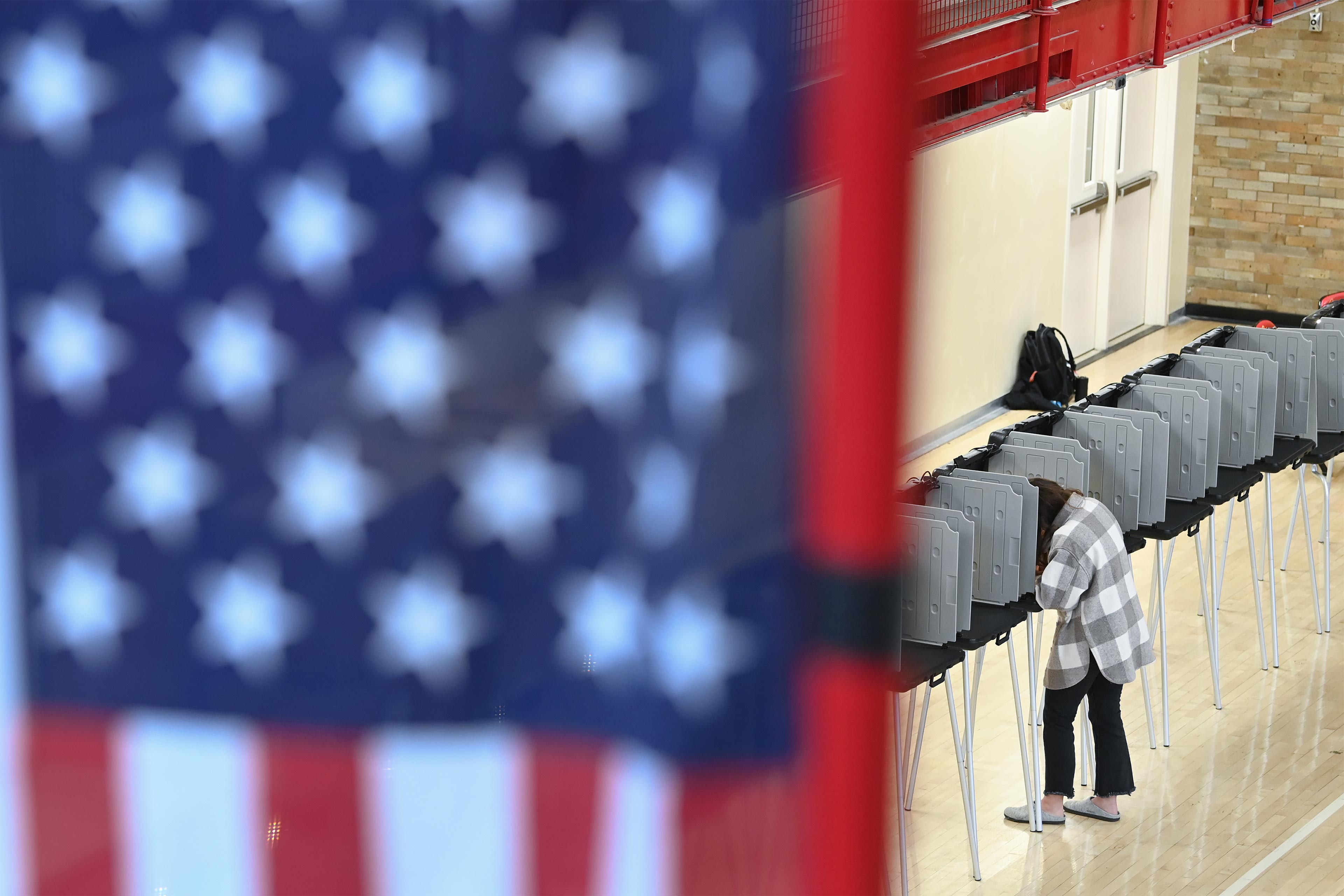 A photo shows a woman at a polling booth, filling out a ballot. A blurred American flag is seen in the photo's foreground.