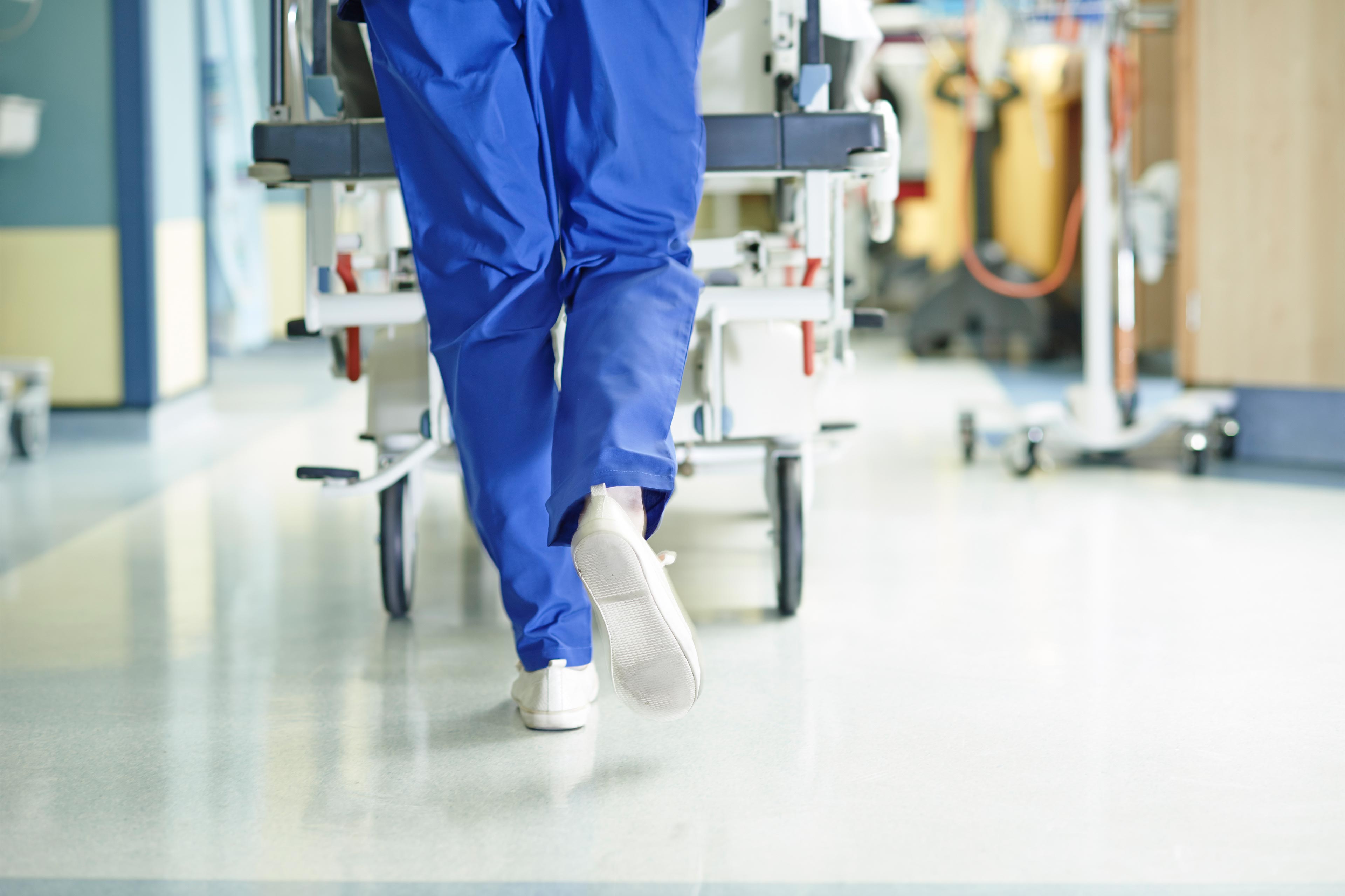 A photo shows a nurse's legs walking through a hospital corridor while pushing a gurney.