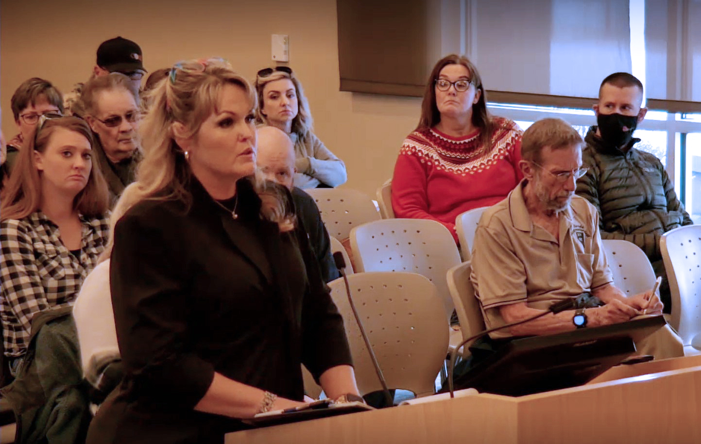 A photo shows Abigail Wheeler speaking into a microphone at a county commission meeting.