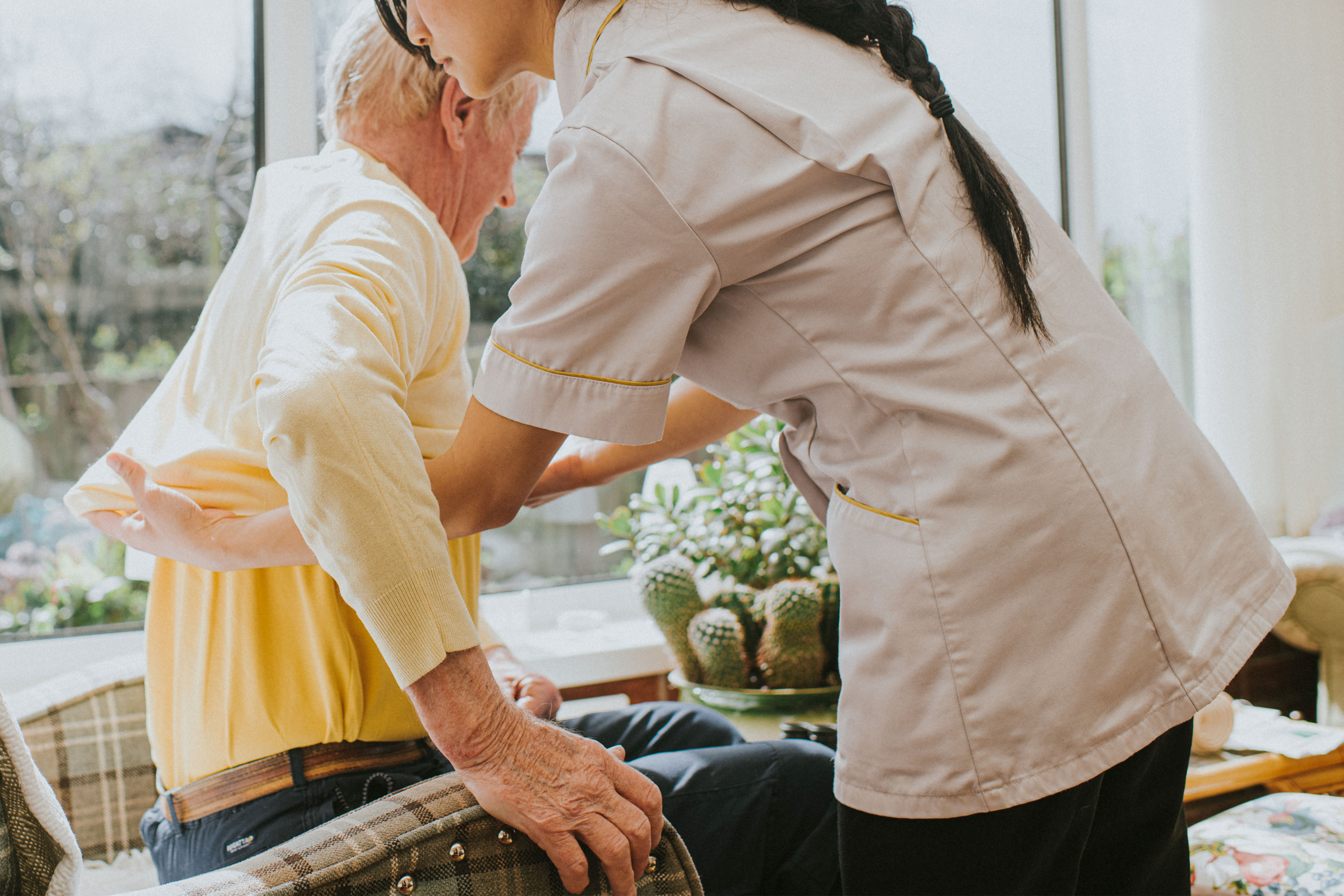 A photo shows a woman caregiver helping an elderly man get dressed.
