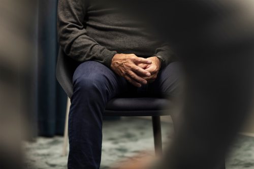 A shows a man's mid-section, sitting in a chair with his hands together.