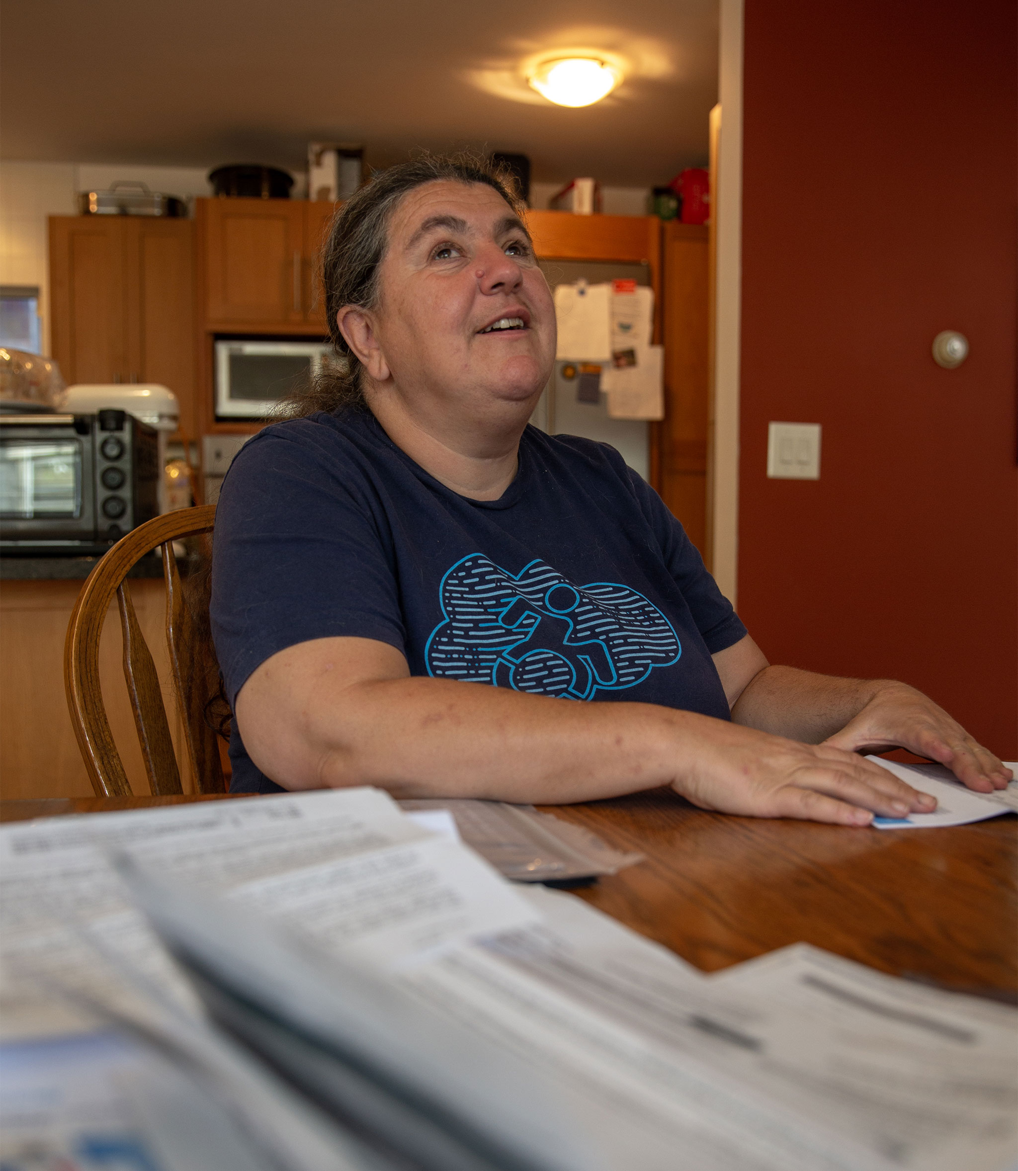 A blind woman sits at a dining table next to a pile of open mail and feels a piece of paper with her hands.