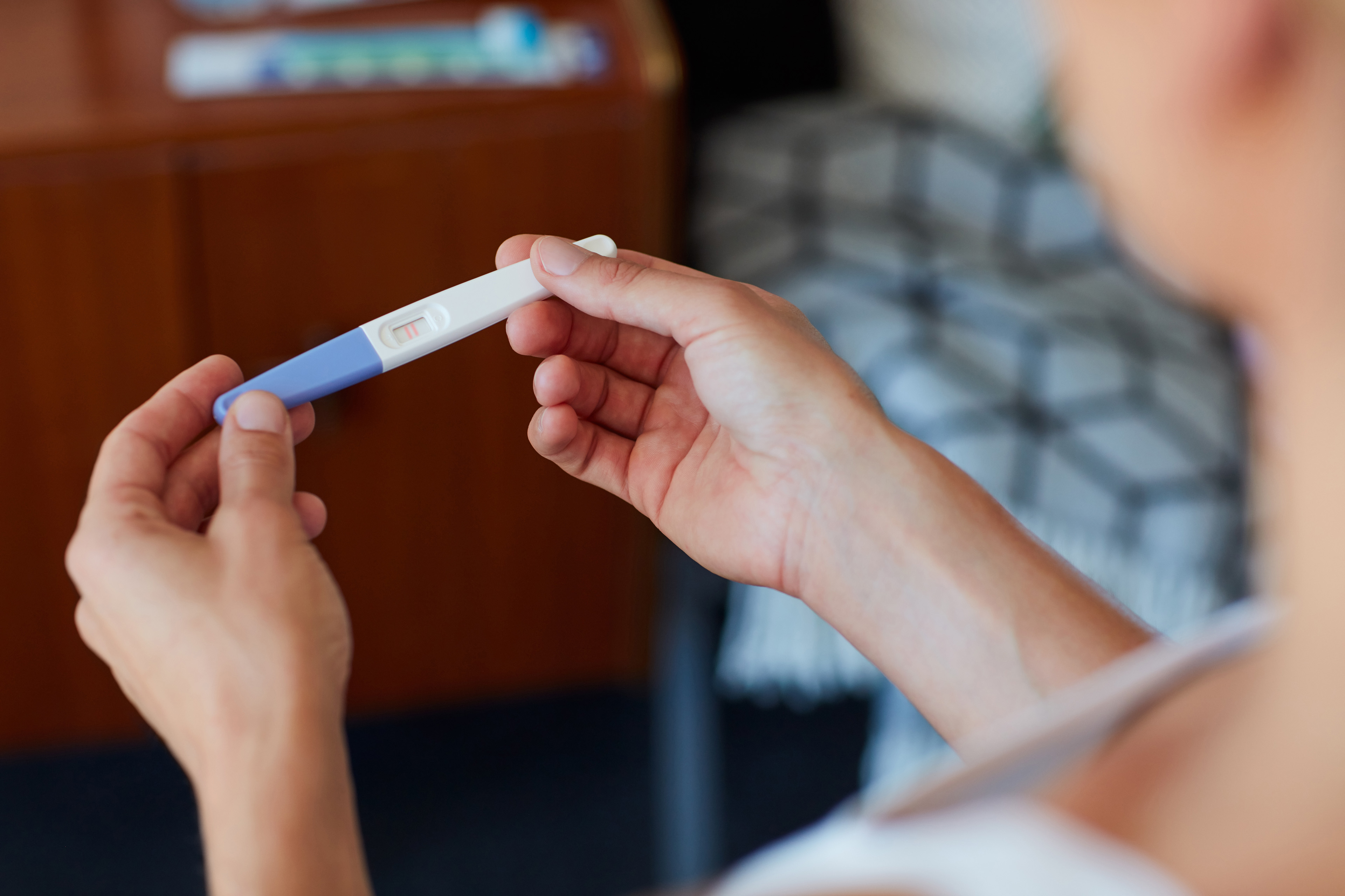 High angle shot of an unrecognizable young woman holding a pregnancy test in her bedroom at home.