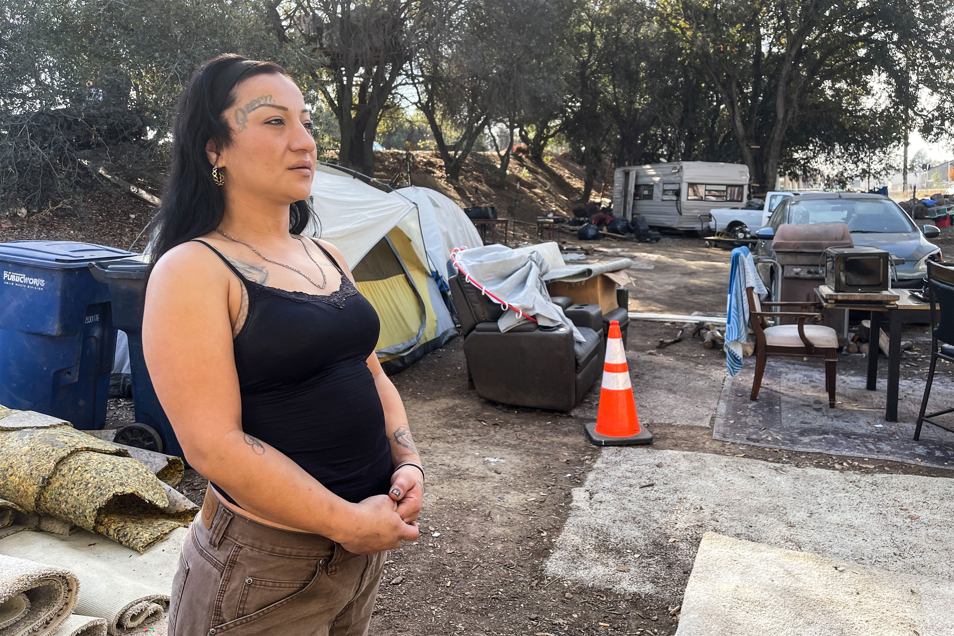 A photo shows Daisy Gonzalez posing for a portrait outside near the encampment where she lives.