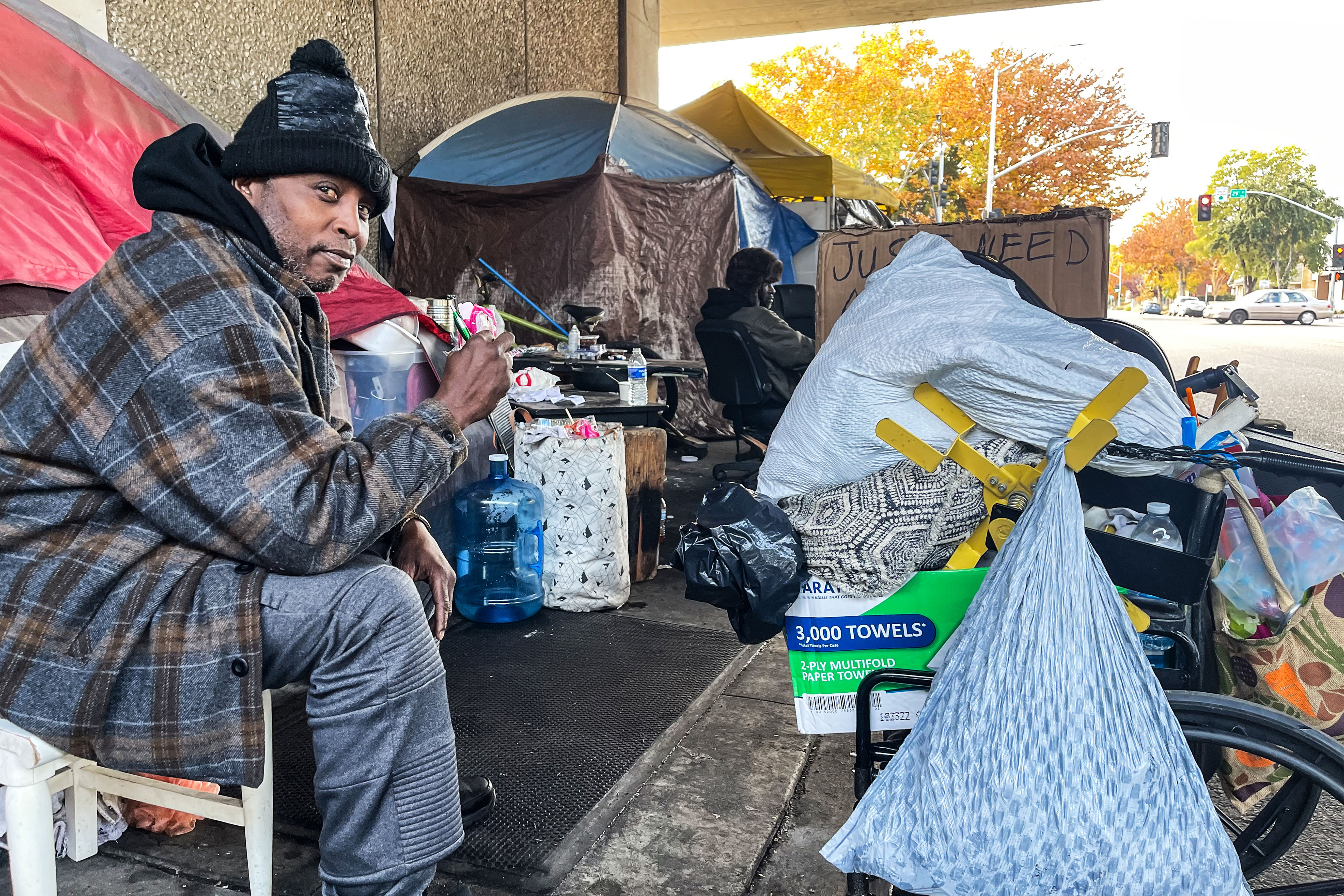 A photo shows Chilli Williams sitting at the homeless encampment under a freeway where he lives.