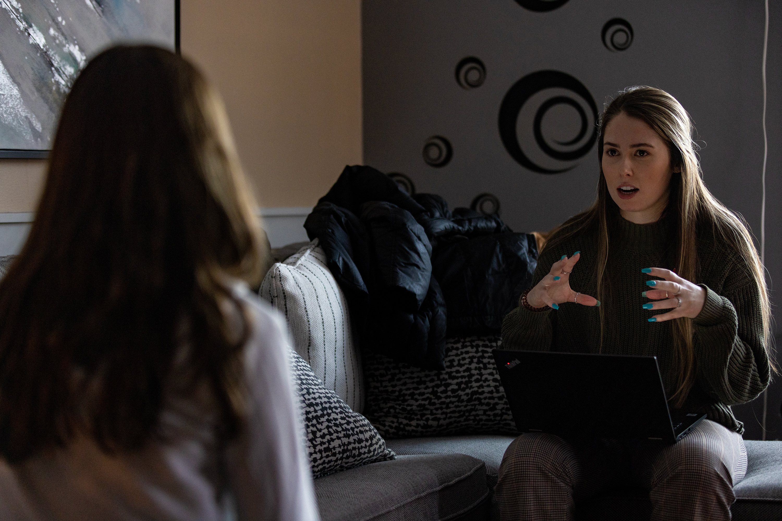 Laura Polizoti, a family intervention specialist, is sitting on a couch across from her patient, as they talk. The patient faces away from the camera, so their face cannot be seen.