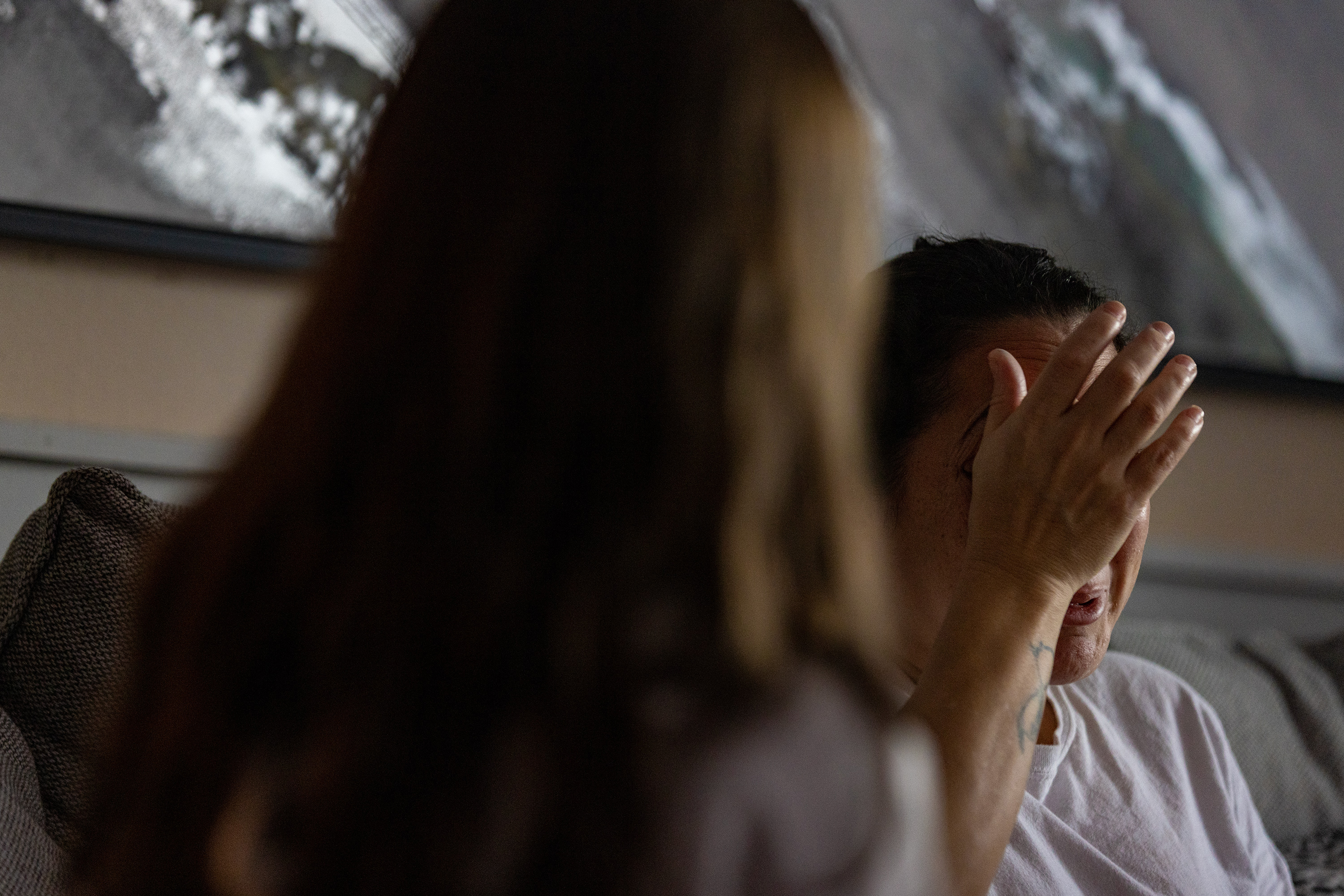 Haley's mother covers her face with her hand as she talks. She is sitting beside her daughter on a couch; her daughter is facing away from the camera.