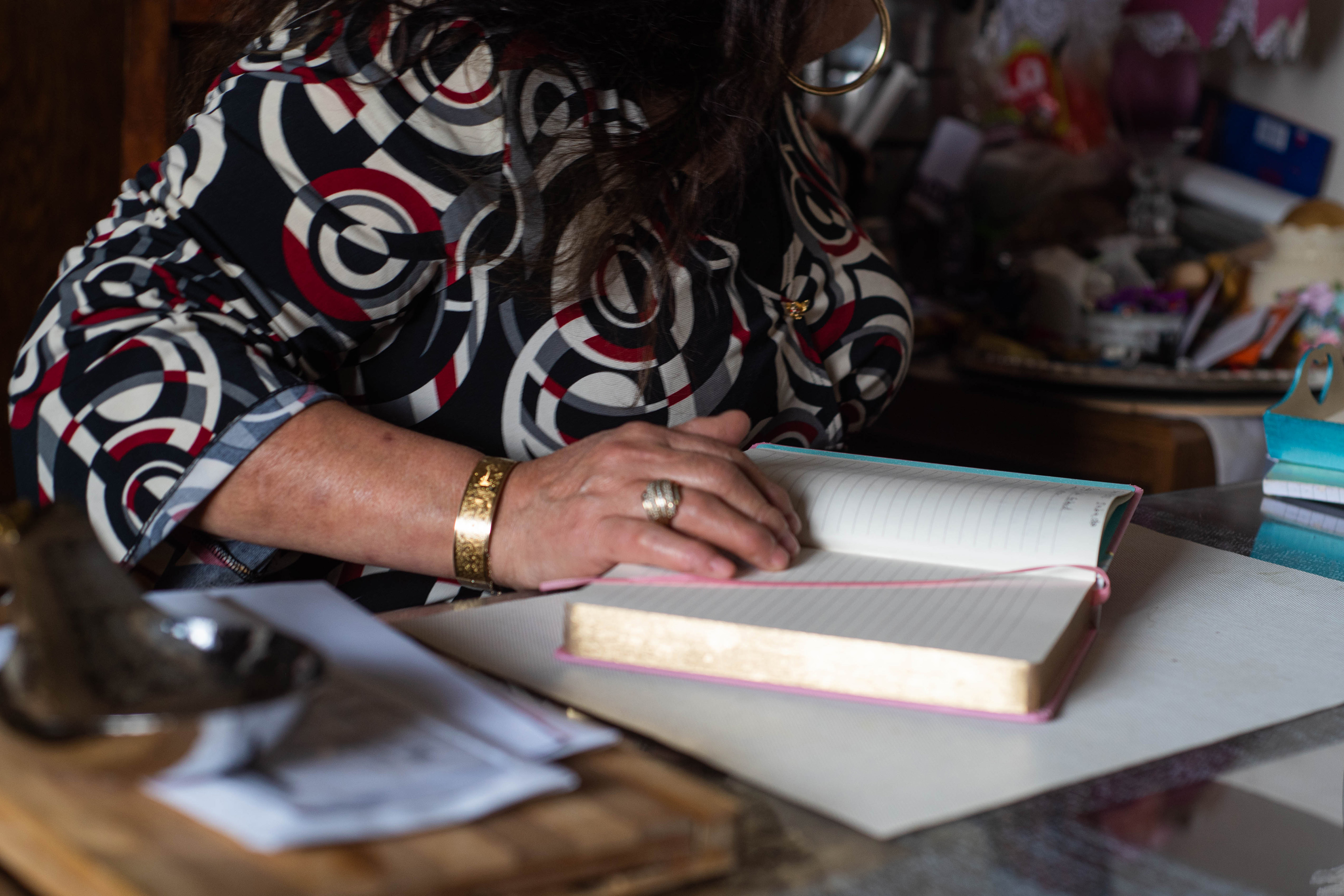 Bertha Embriz is seen from the shoulders down as she sits at her desk. Her hand rests on her notebook, which is open.