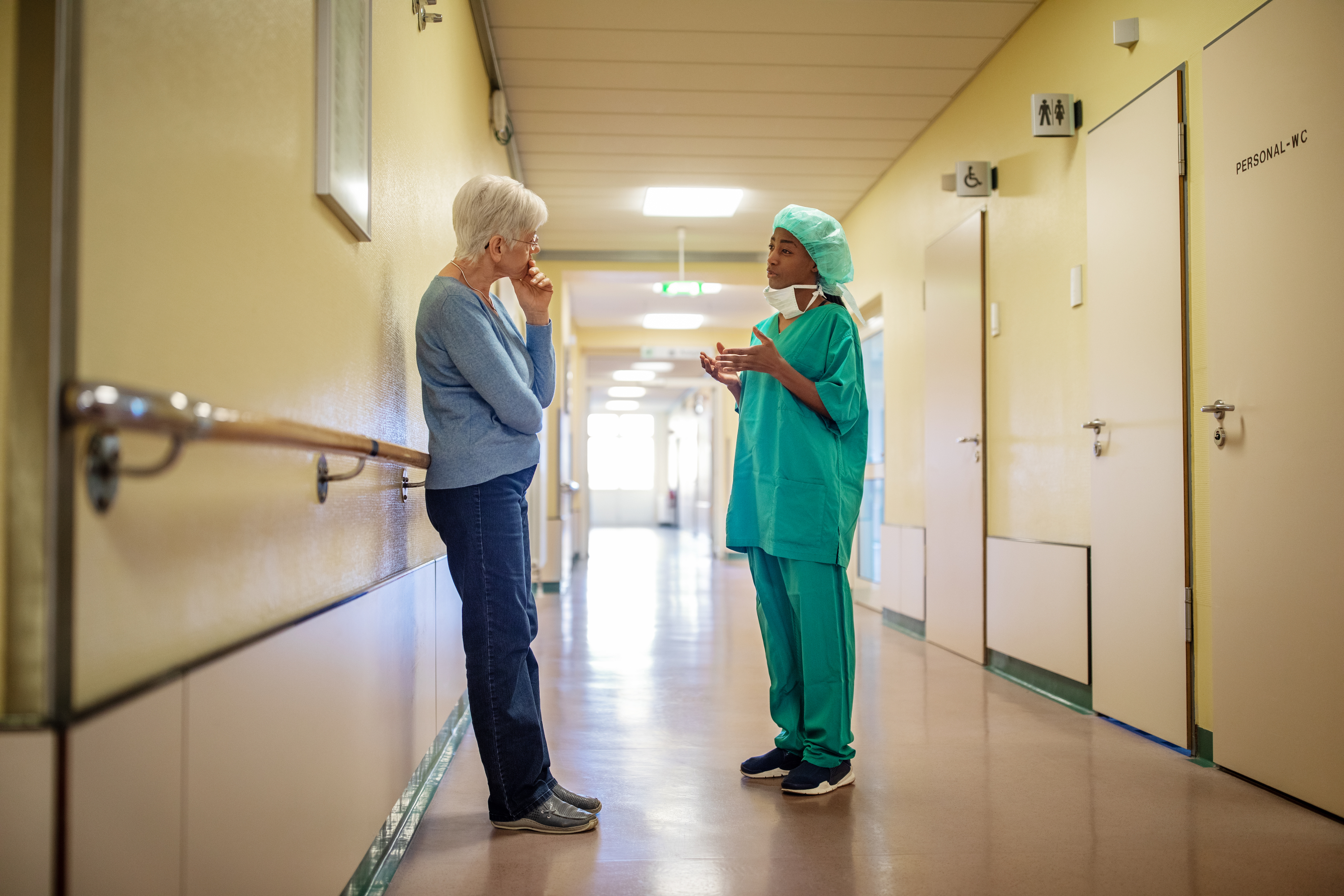 Female surgeon in scrubs talking with senior woman in hospital corridor. Surgeon talking with woman in hallway at hospital.